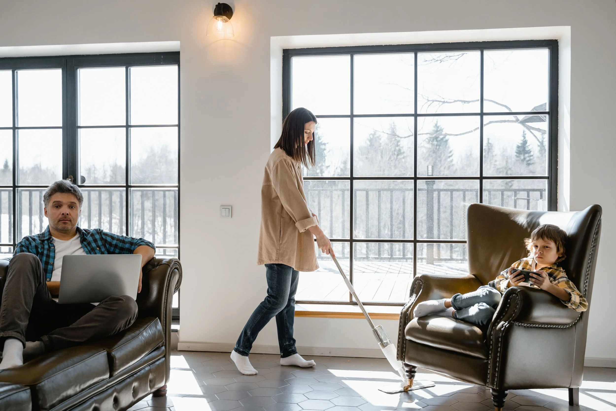 Two people in a shared space with one actively managing tasks while the other is disengaged, representing the overfunctioning and underfunctioning dynamic in couples