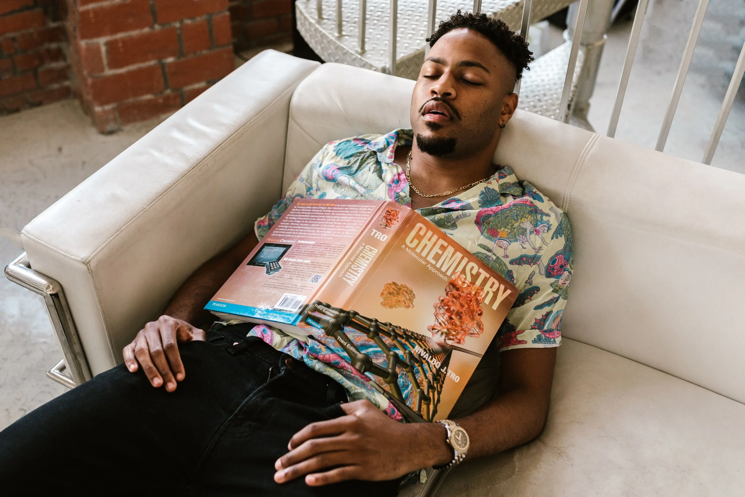 A fully dressed person lying on a couch with eyes closed and a phone resting on their chest, representing burnout and exhaustion in high-functioning adults