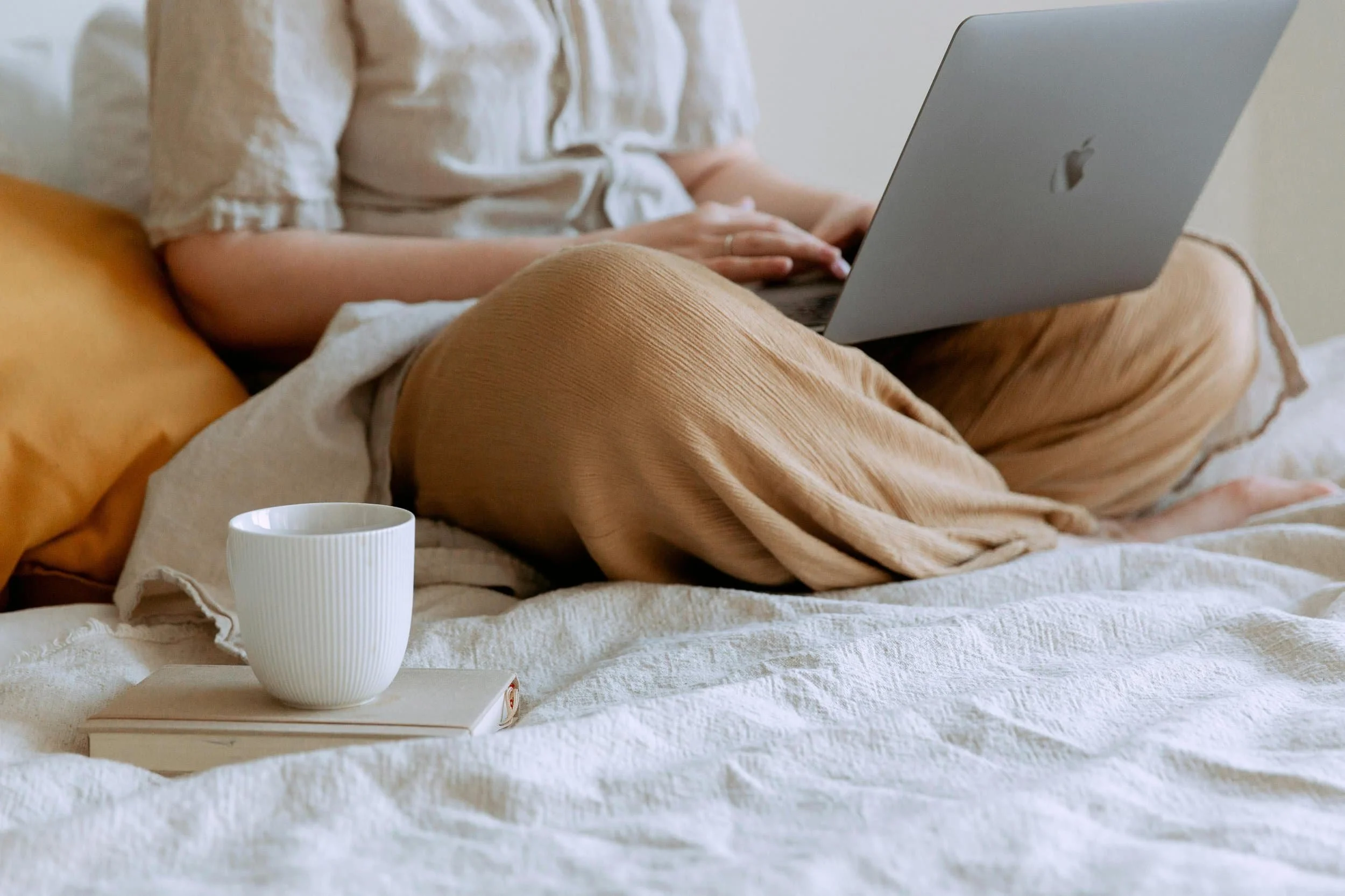 A person sitting cross-legged on a bed with a laptop and a cup of coffee, representing telehealth therapy access in Connecticut