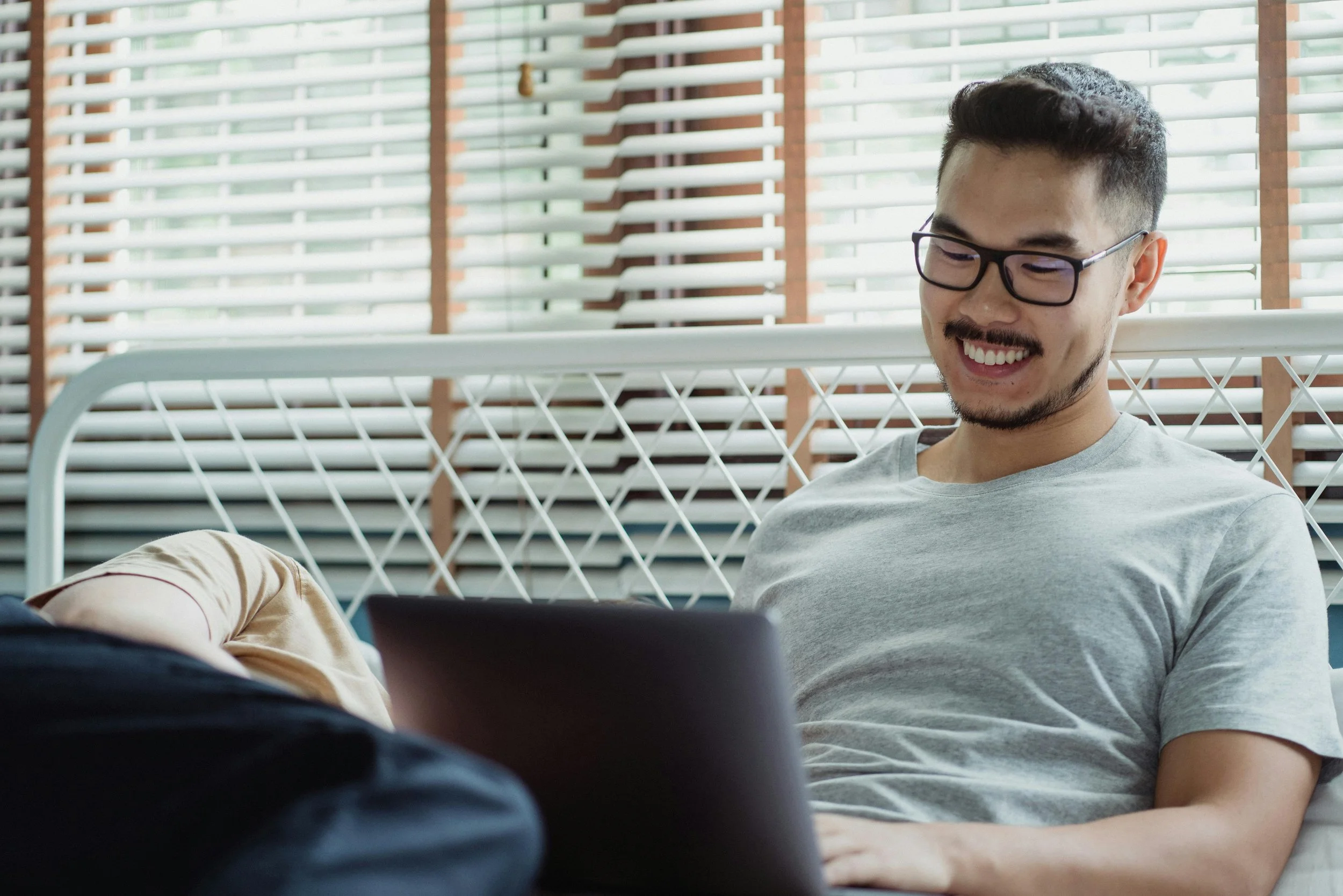 A man smiling while working on a laptop by a window, representing boundary setting and identity therapy for adults in Connecticut
