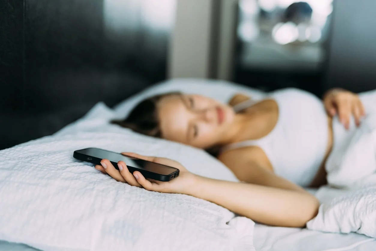 A phone screen lit on a nightstand beside someone trying to sleep, representing the always-on expectations driving functional burnout in adults