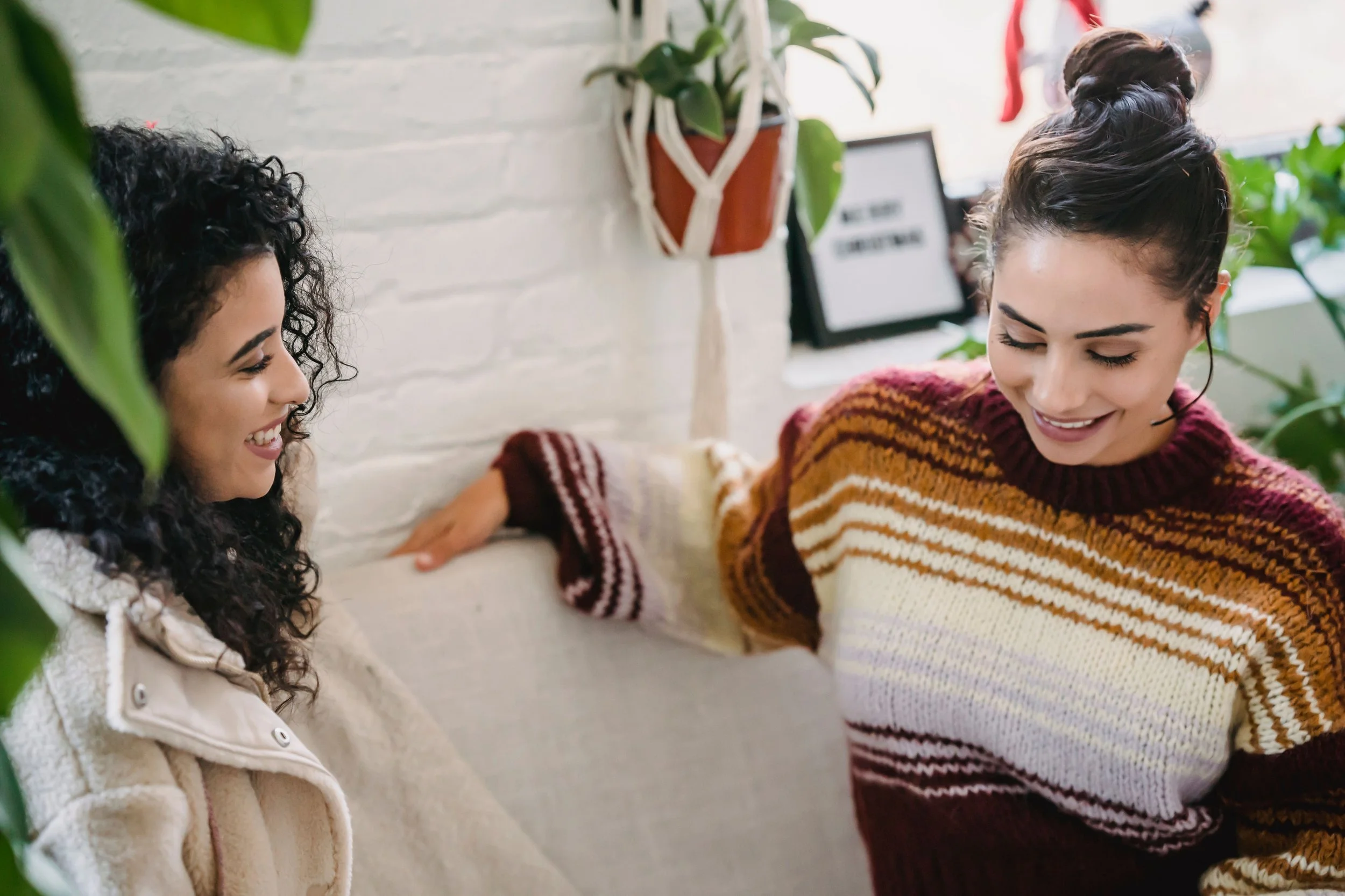 Two women facing each other in a warm domestic setting having an honest conversation, representing the work of breaking generational patterns while preserving family connection
