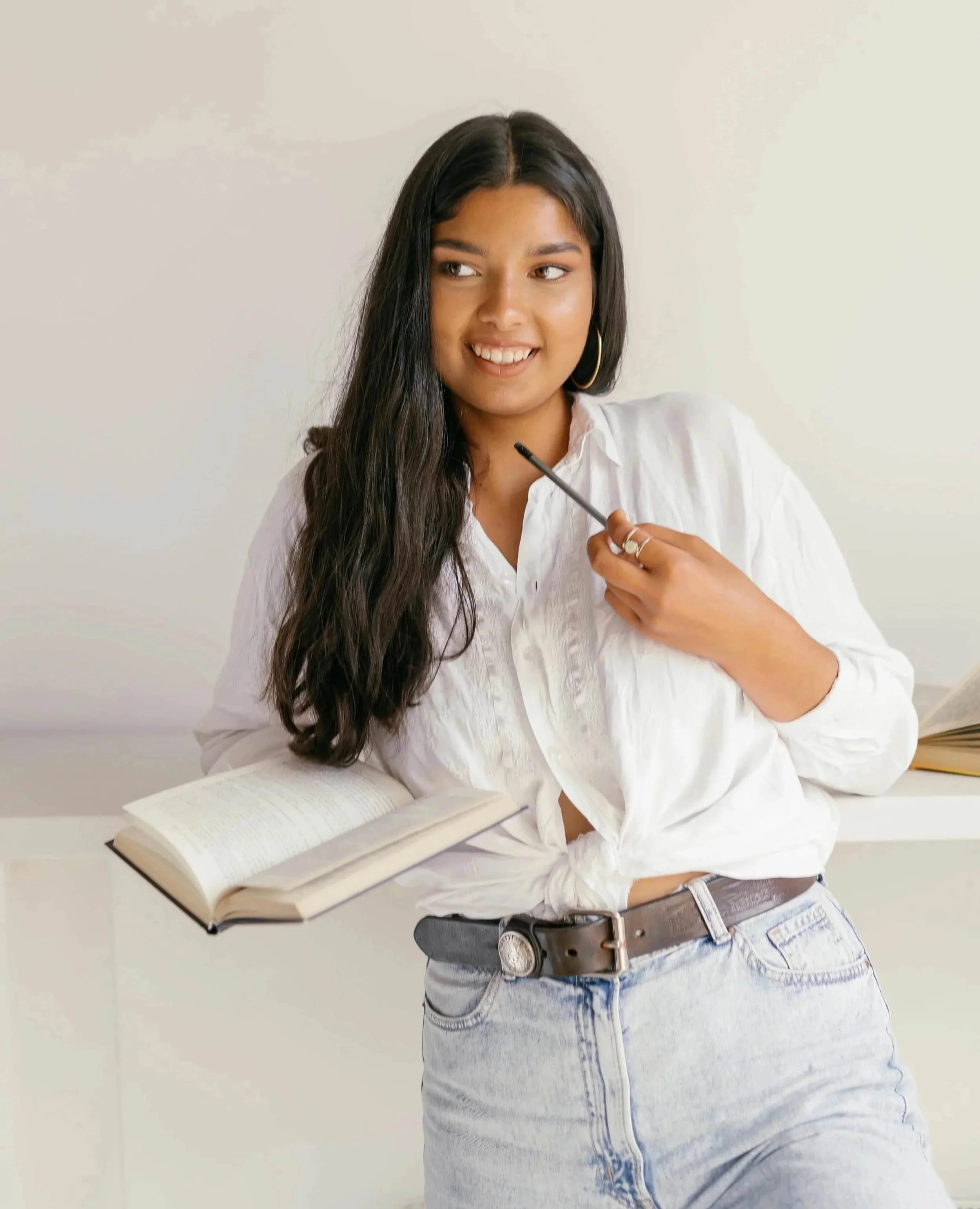 A young woman holding a pencil and an open journal, smiling and looking away thoughtfully