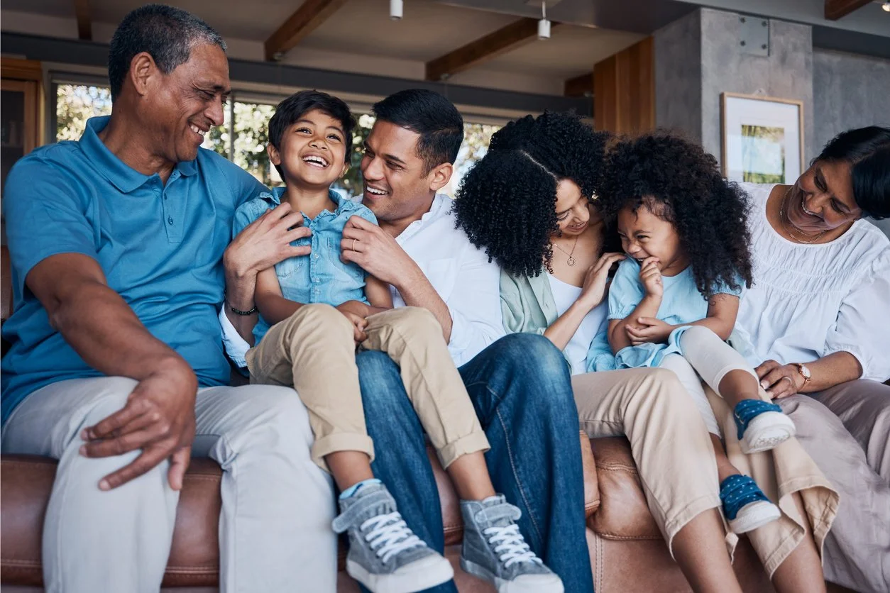 A multigenerational family laughing together on a couch, representing generational patterns therapy in Connecticut