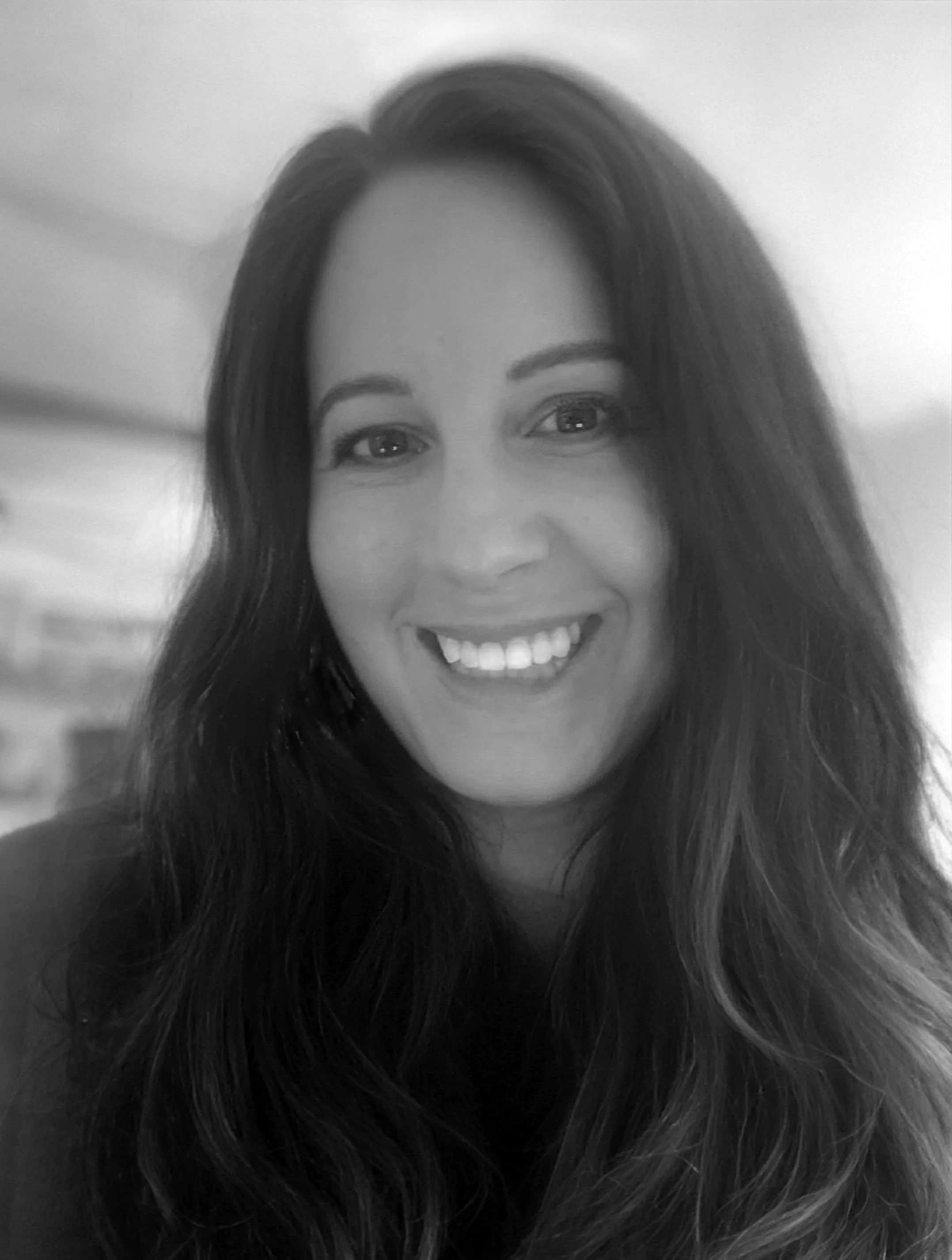 A woman with long, wavy hair smiling at the camera in a grayscale photo.