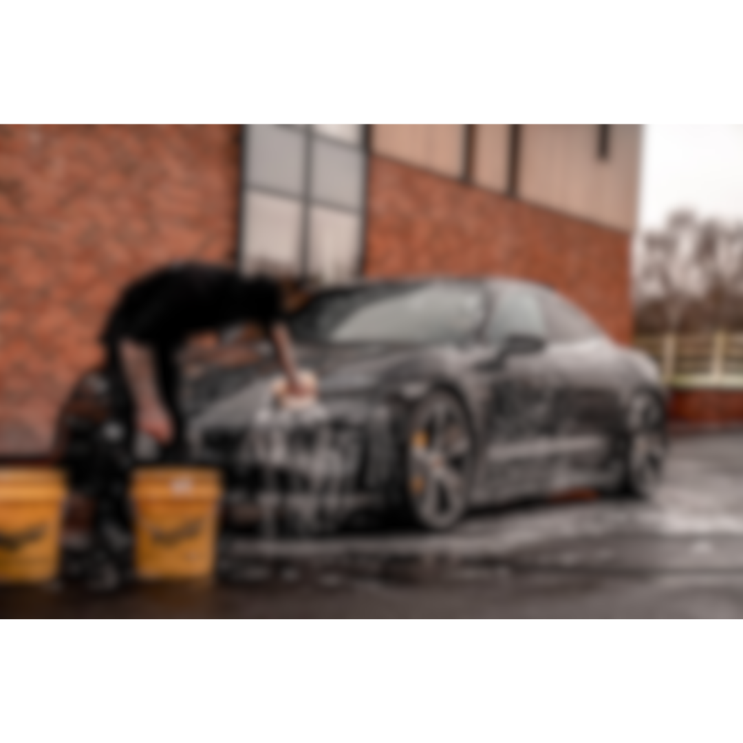 A detailer washing a black sports car with snow foam on a drive way