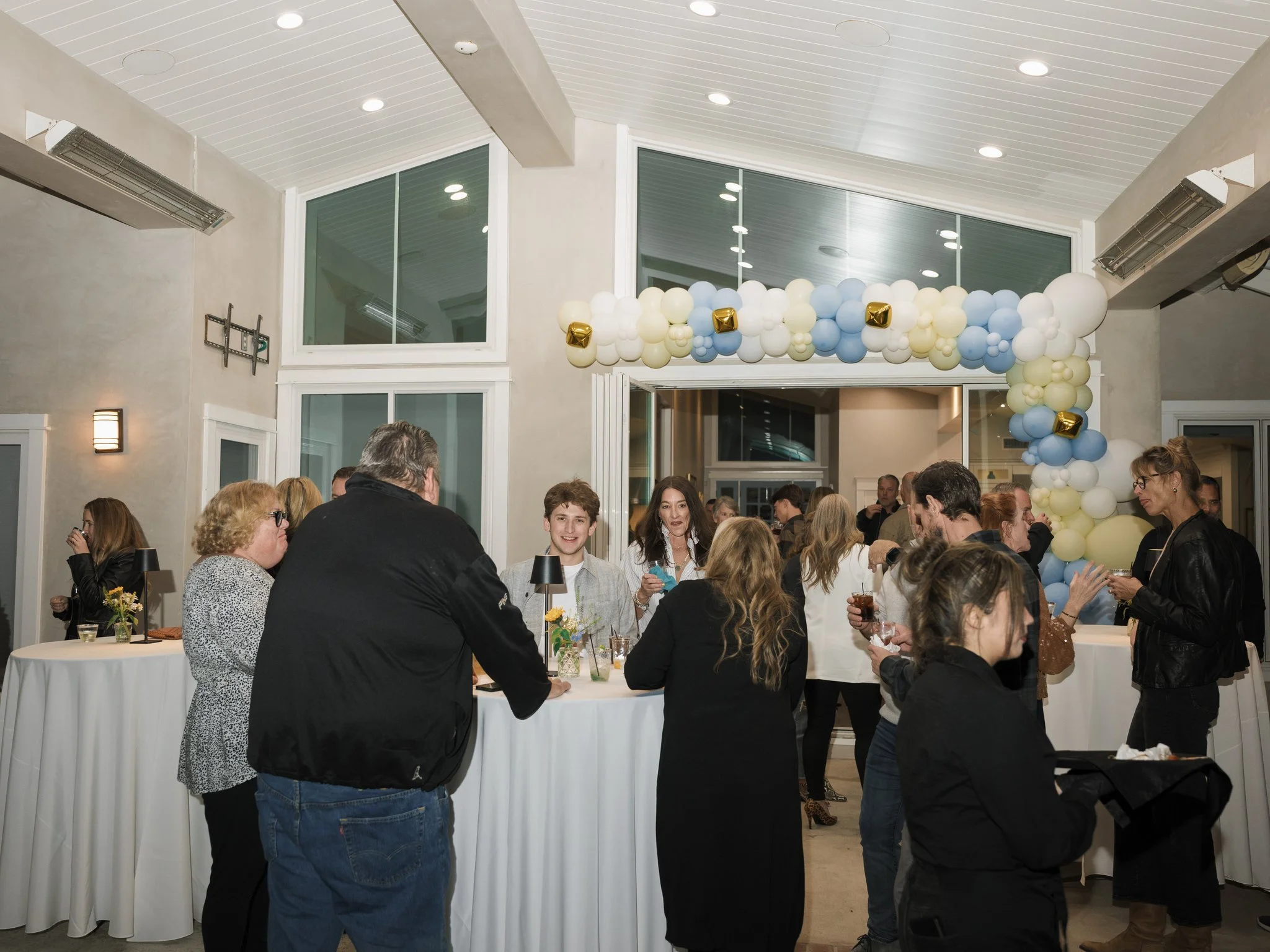 People socializing at a cocktail party under a balloon arch decoration in an indoor event space