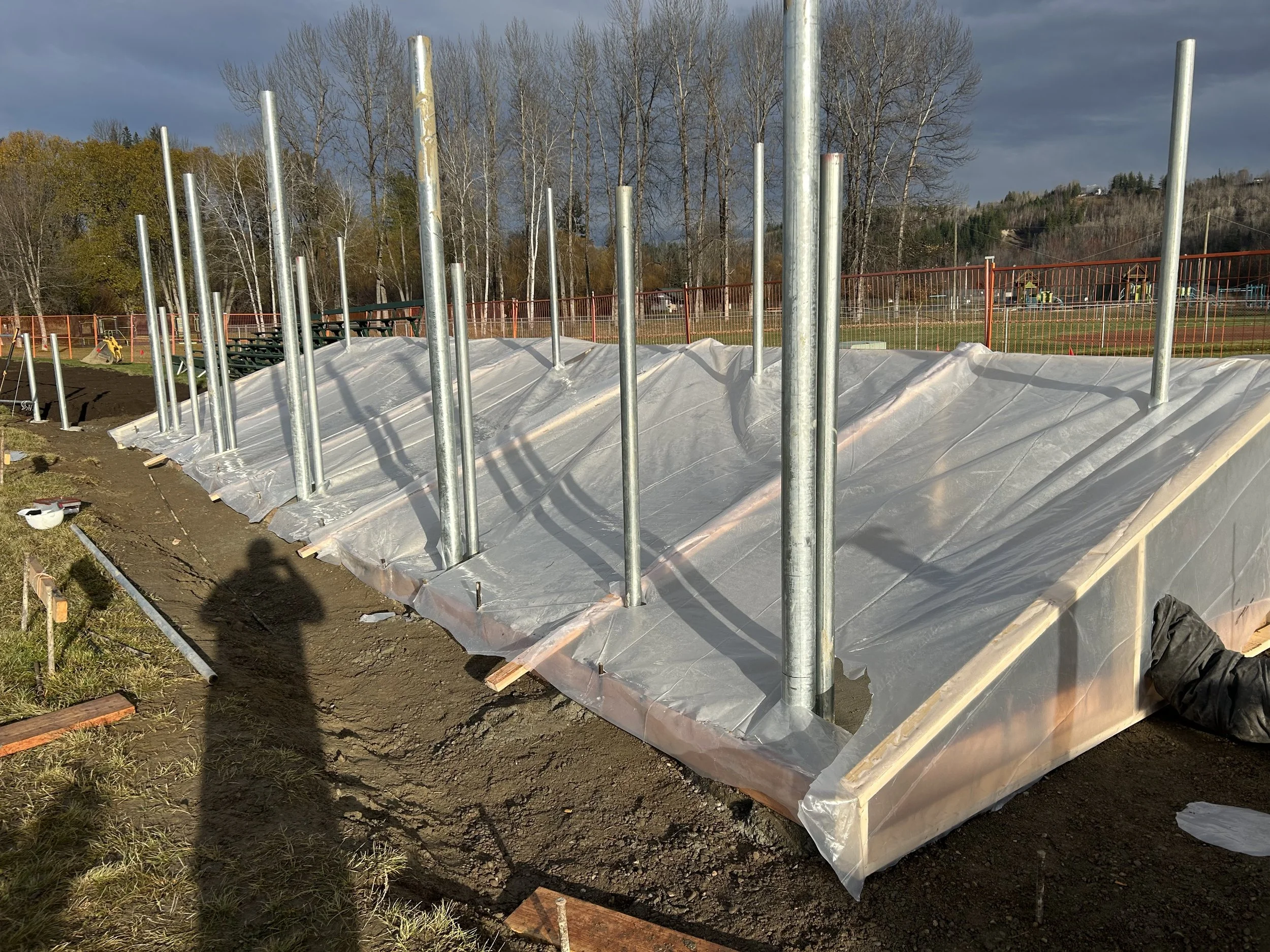 Construction site with a foundation covered in plastic sheeting and metal support poles for a building.