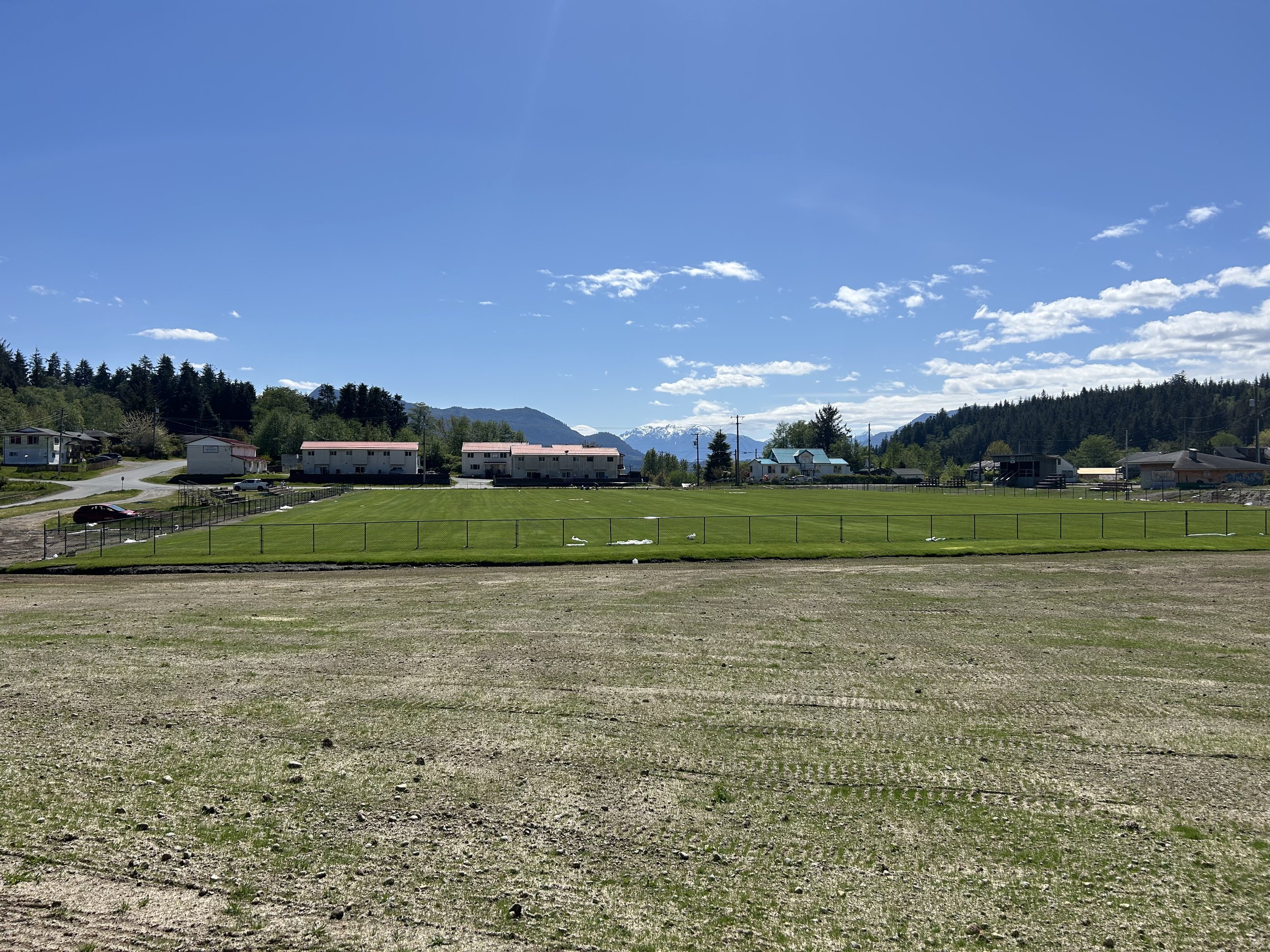 A wide view of a residential area with multiple houses, green lawns, and distant mountains under a partly cloudy blue sky.