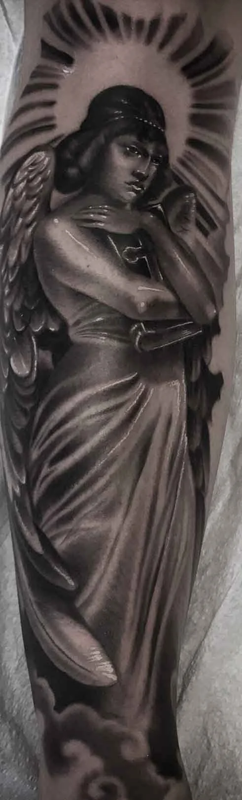 a statuesque angel figure standing in the clouds and a halo behind her black and grey tattoo