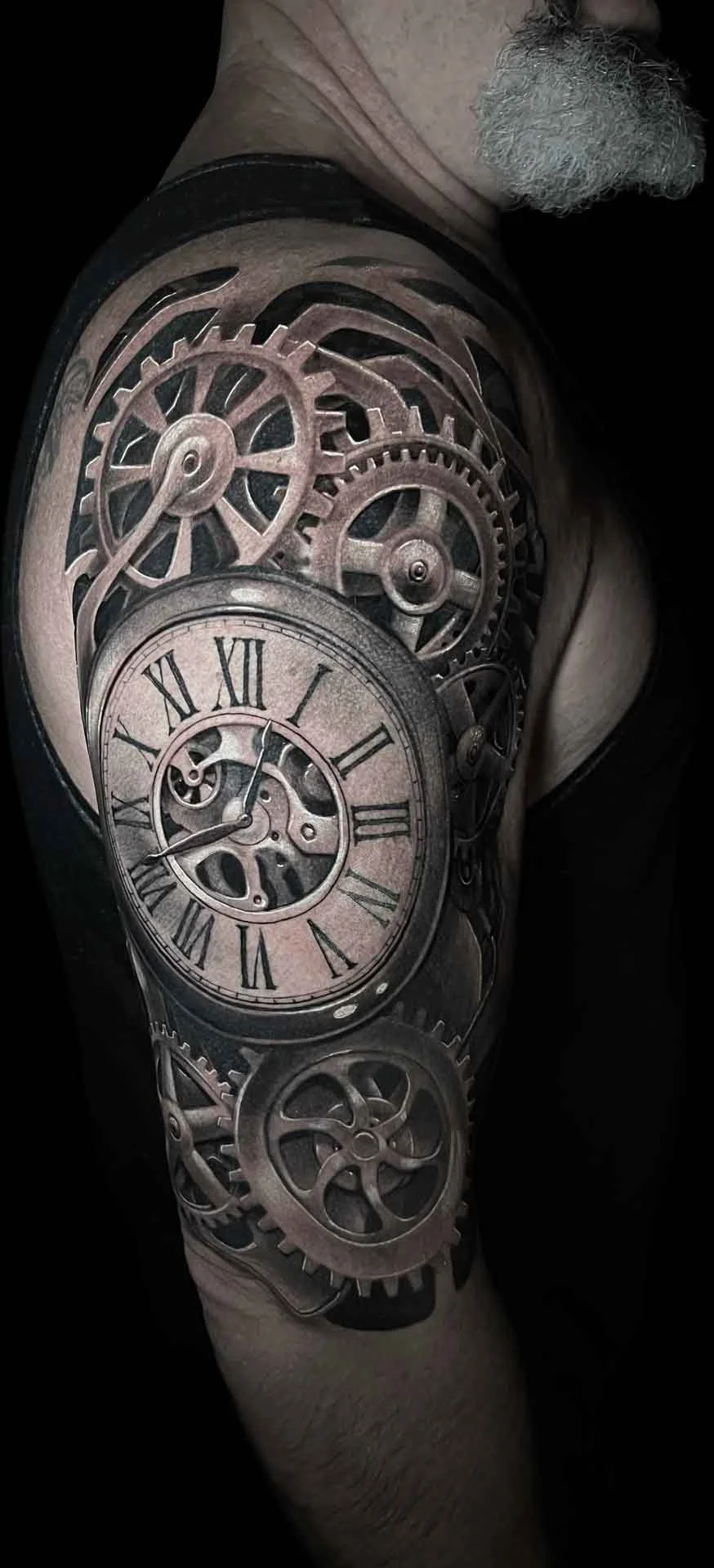A bio-mechanical black and grey hyper realistic gears and clock tattoo on an upper half sleeve by artist Jewp
