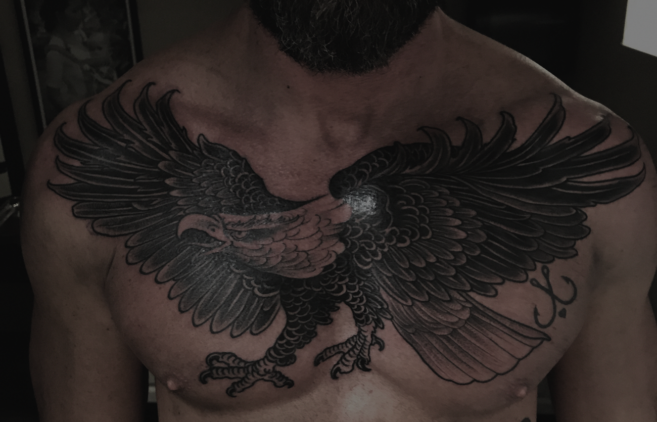 A massive bald eagle tattoo across a man's chest in black and gray don't work illustrative style done by Jewp