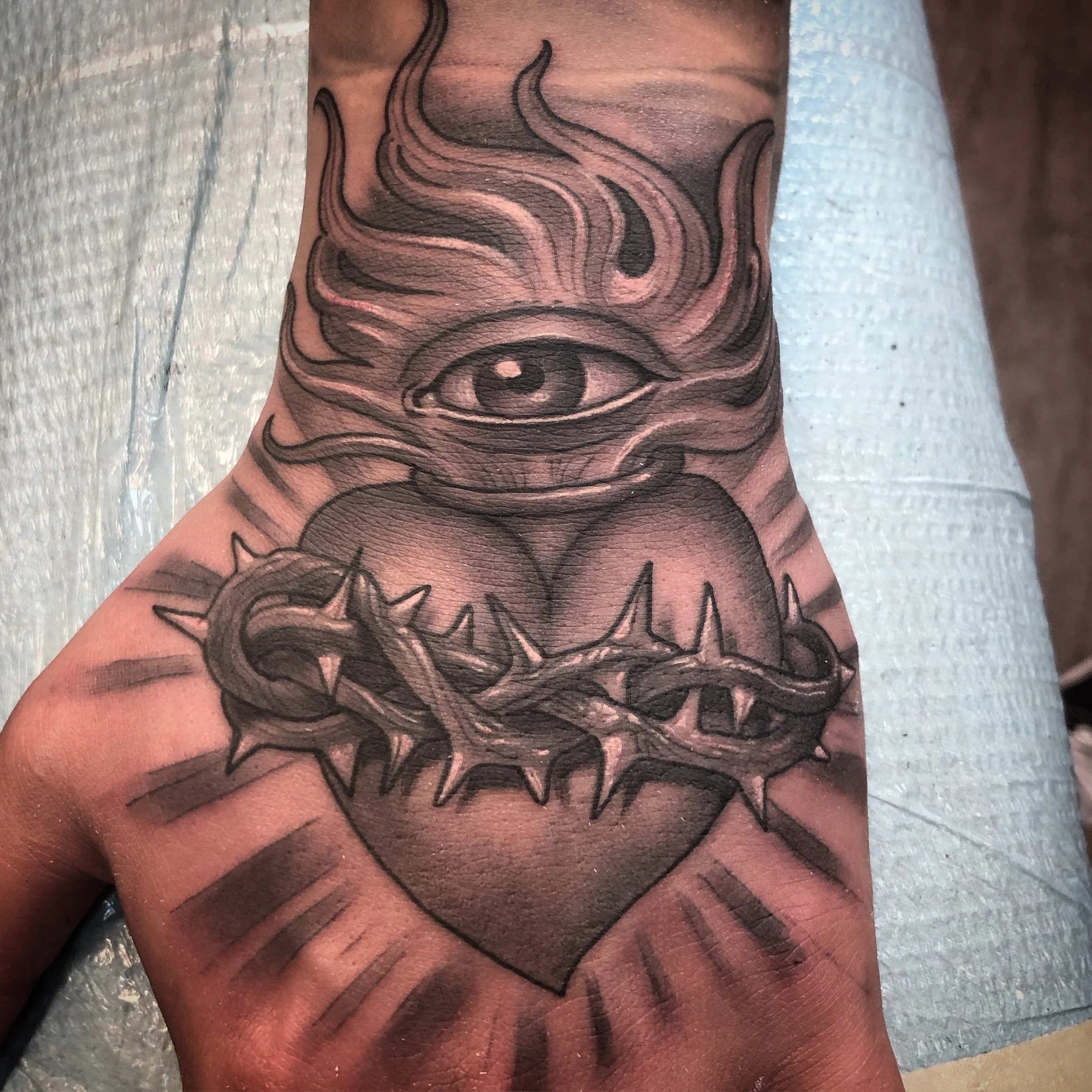 A black and gray immaculate heart tattoo on a hand 