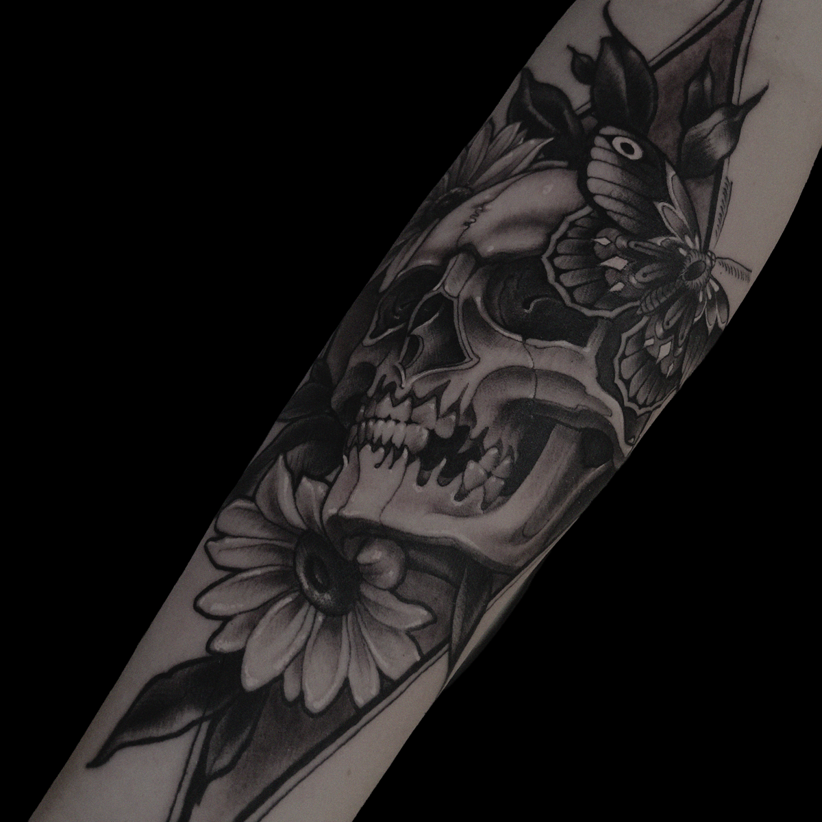 Illustrated in the traditional black work tattoo of a skull, butterfly and floral embellishments on a forearm done by Jewp
