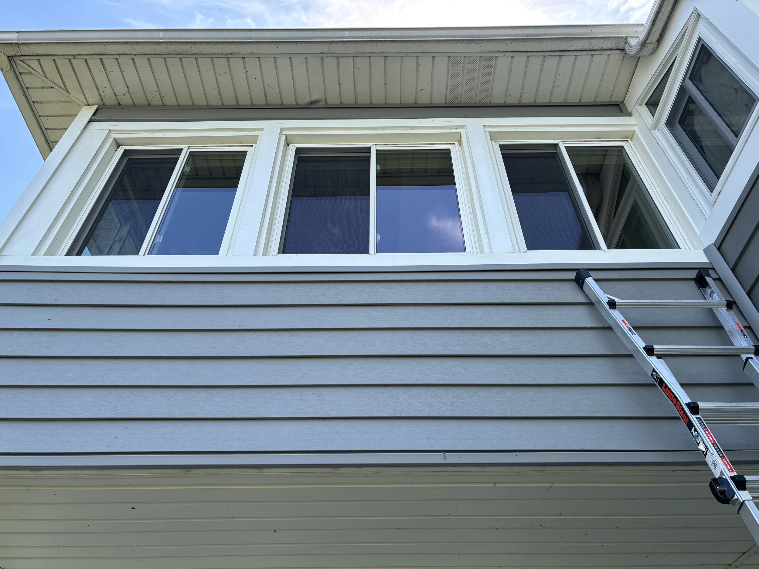 Exterior view of a house with a set of large windows and a ladder leaning against the wall.