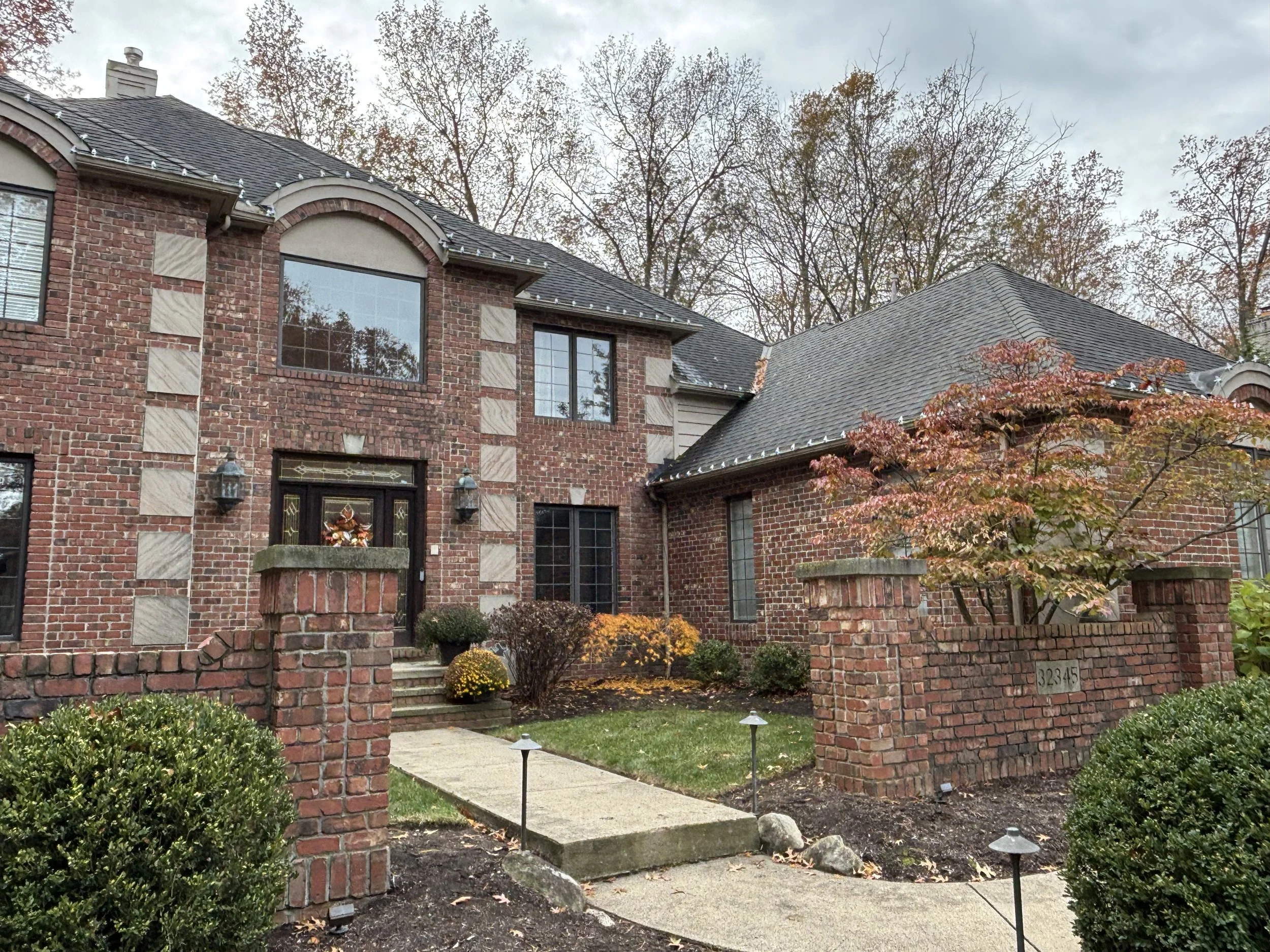 Brick house with a front yard, pathway, trees, and shrubs during fall.