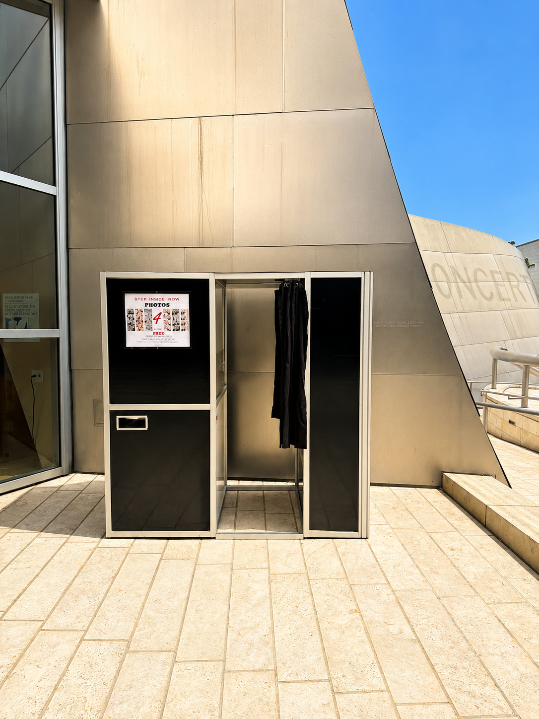 Photo booth with black curtains in front of modern building with beige walls and a clear blue sky.