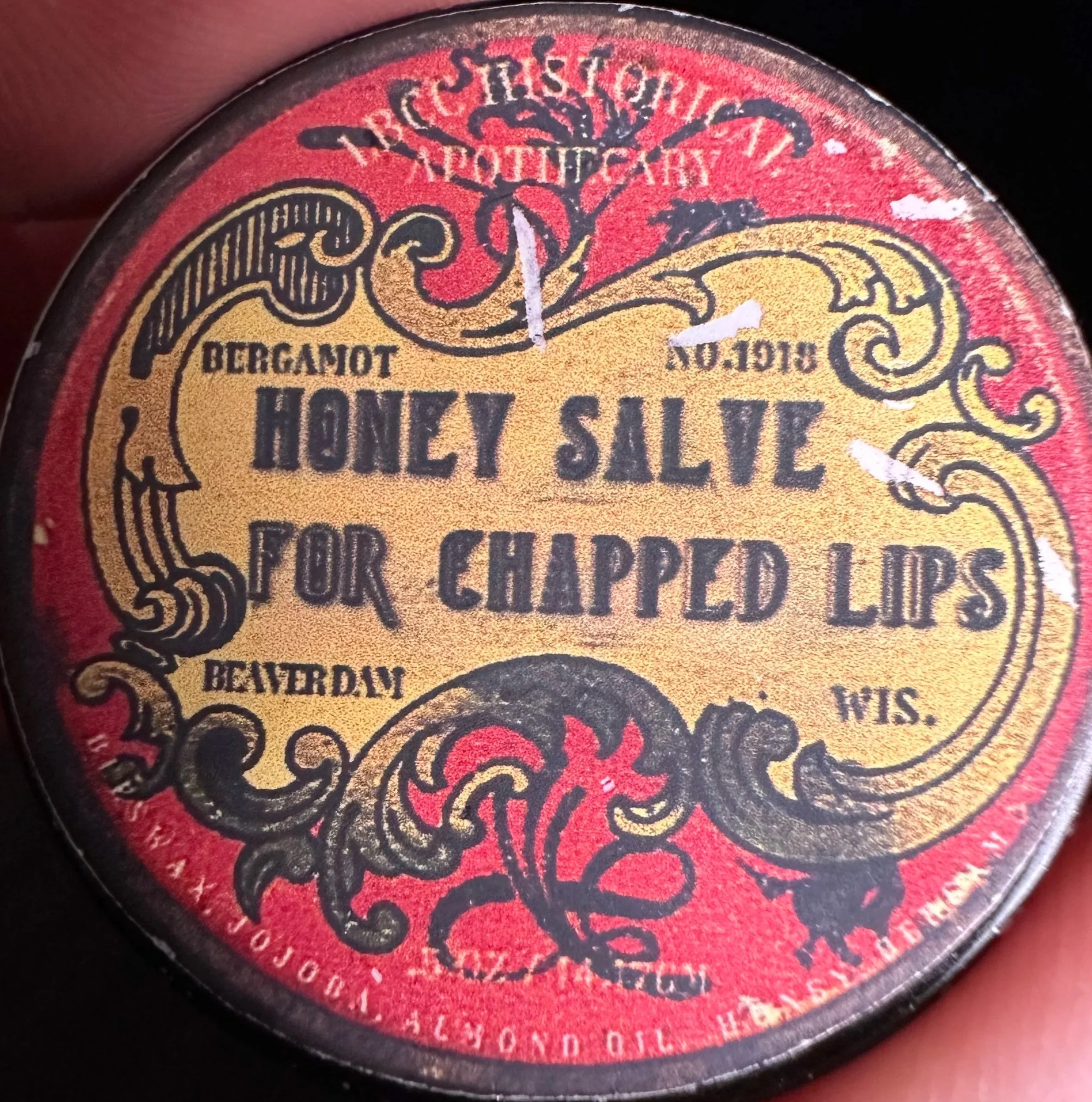Vintage round tin with yellow and red label, featuring black ornate decorative lines. Text reads 'Bergamot Honey Silve for Chapped Lips,' and indicates it is from Beaverdam, Wisconsin.