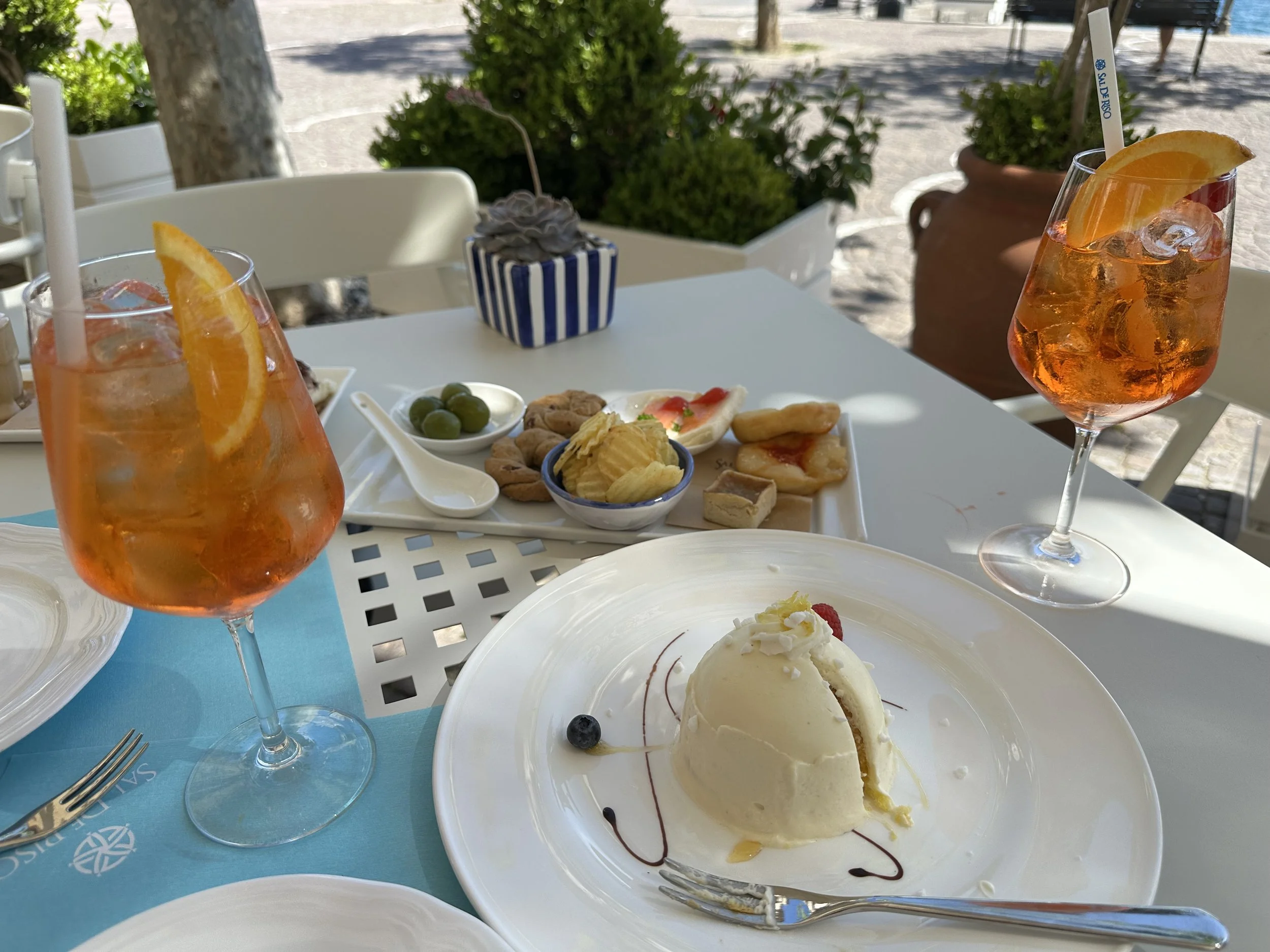 image of a cafe table with two glasses of Aperol spritz, antipasto snacks, and lemon delight desert.