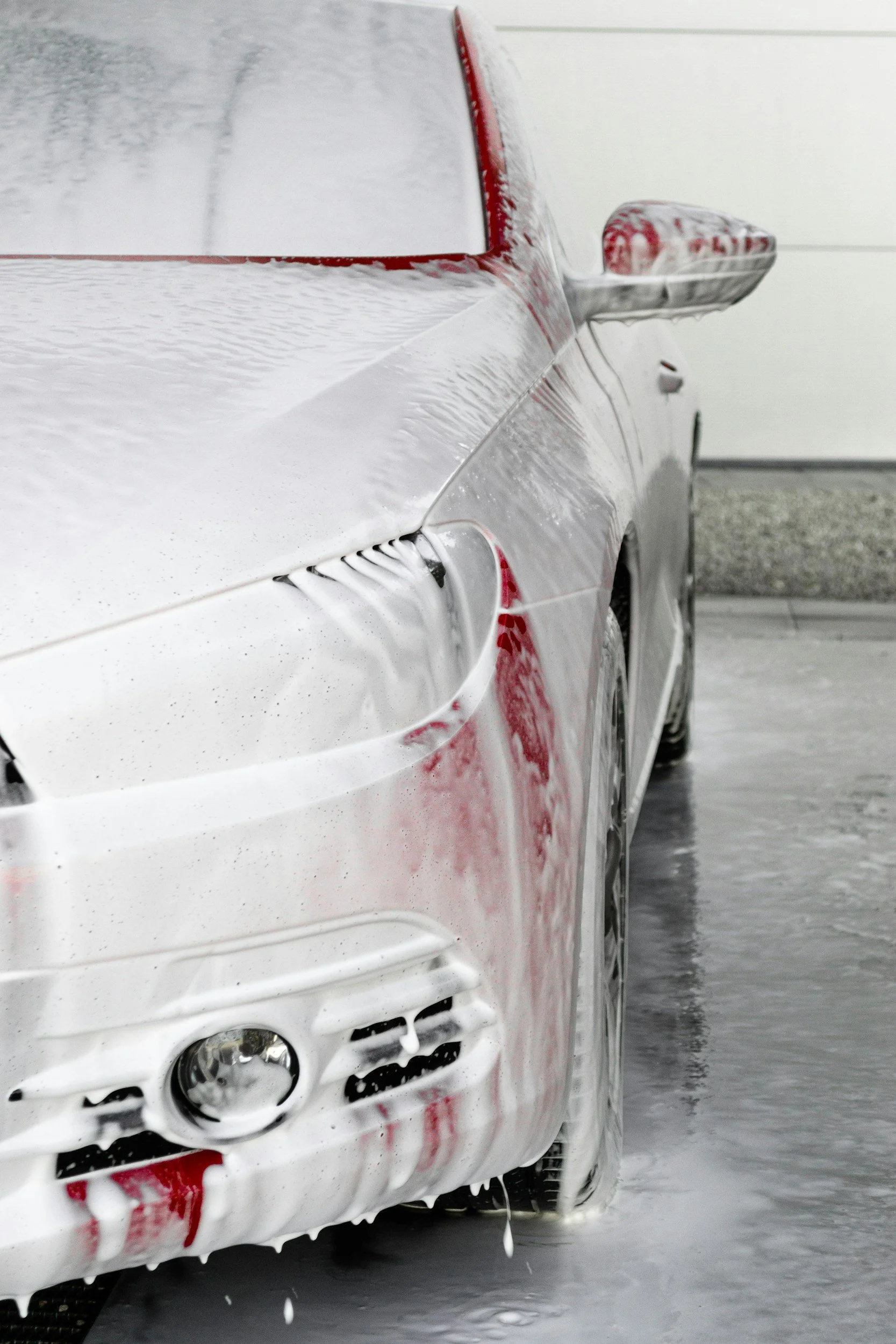 Rear side of a silver car covered in soap and foam during car wash, with soap dripping off.