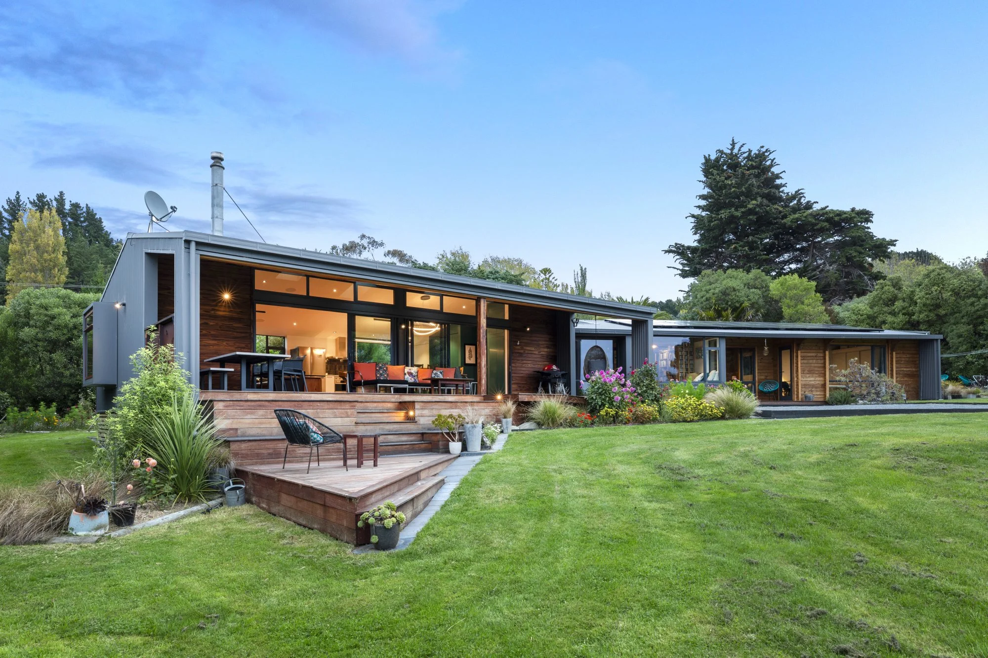 Modern house with large outdoor patio and well-manicured lawn, surrounded by trees and greenery.