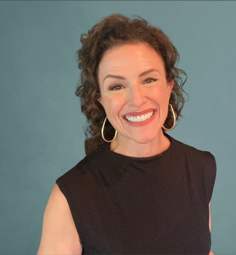 Woman with curly brown hair, wearing hoop earrings and a sleeveless black top, smiling against a teal background.