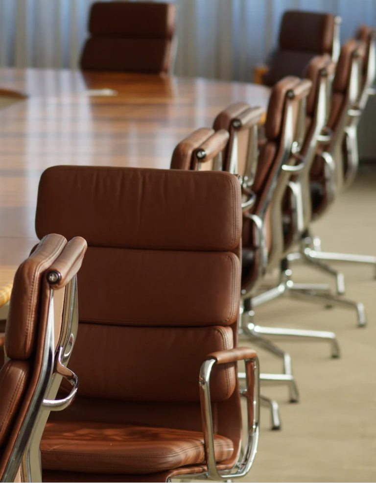 A conference room with a row of brown leather office chairs around a large wooden table.