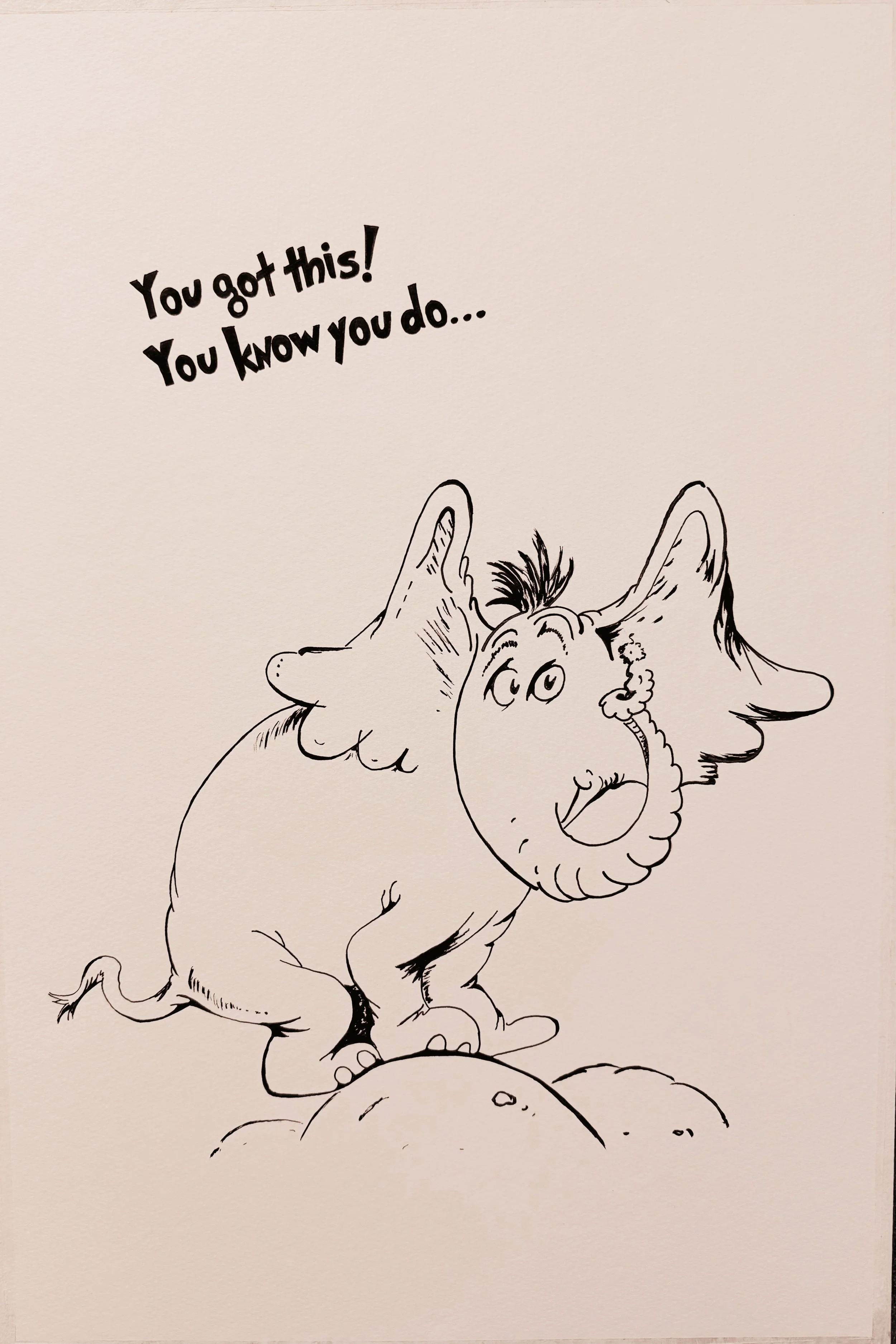 A black and white drawing of a cartoon dragon with large ears, standing on rocks and holding a speech bubble that says, "You got this! You know you do..."