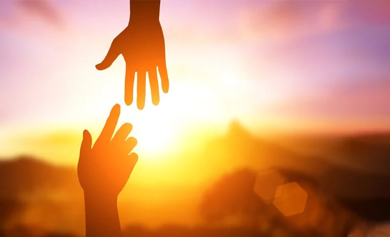 Two silhouetted hands reaching towards each other against a sunset background.