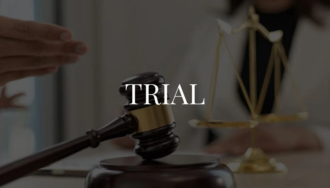 Close-up of a judge's gavel and scales of justice on a desk, with the word 'TRIAL' overlaid.
