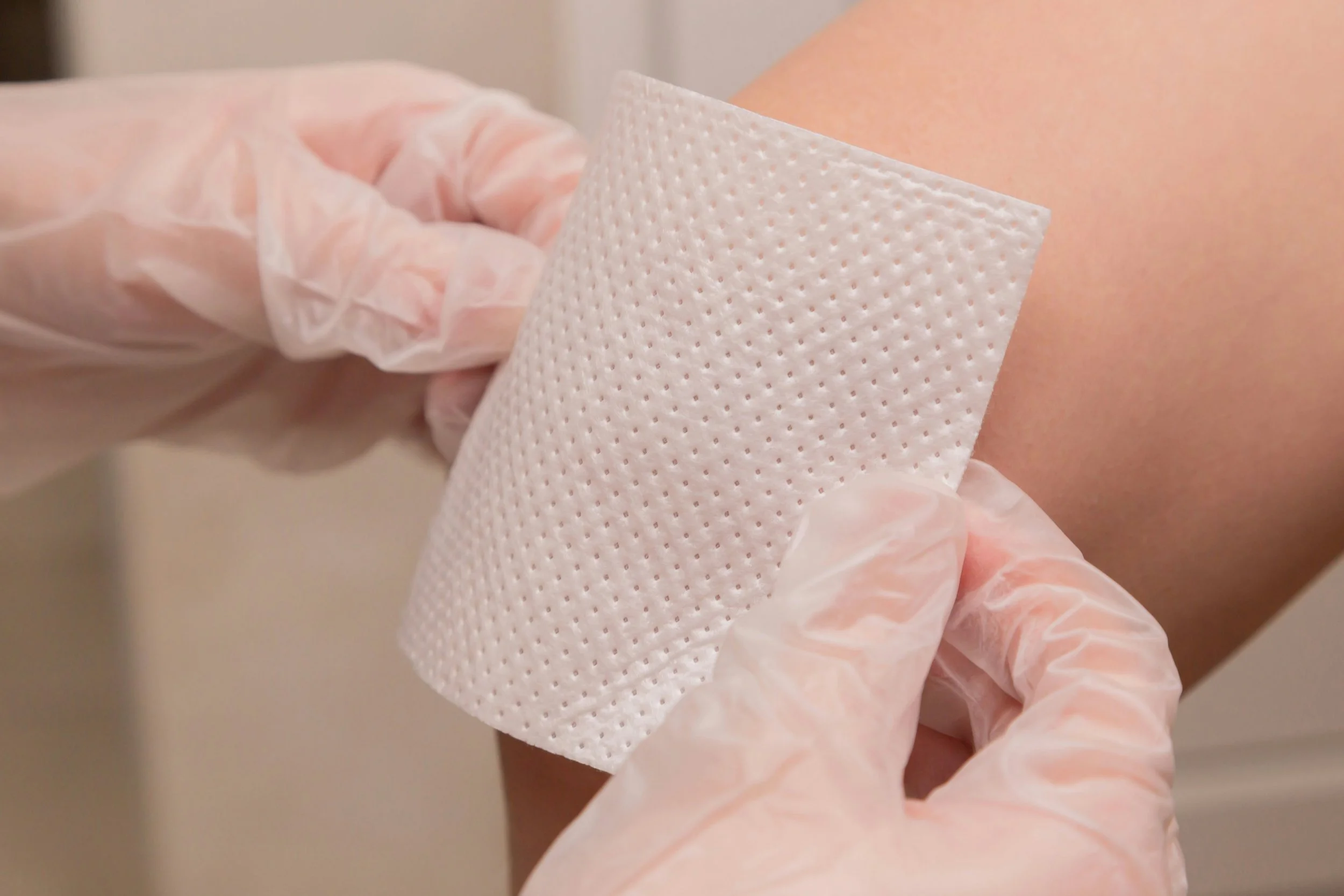 Close-up of a medical professional applying a bandage or adhesive pad on a person's arm. The person is wearing a latex glove.