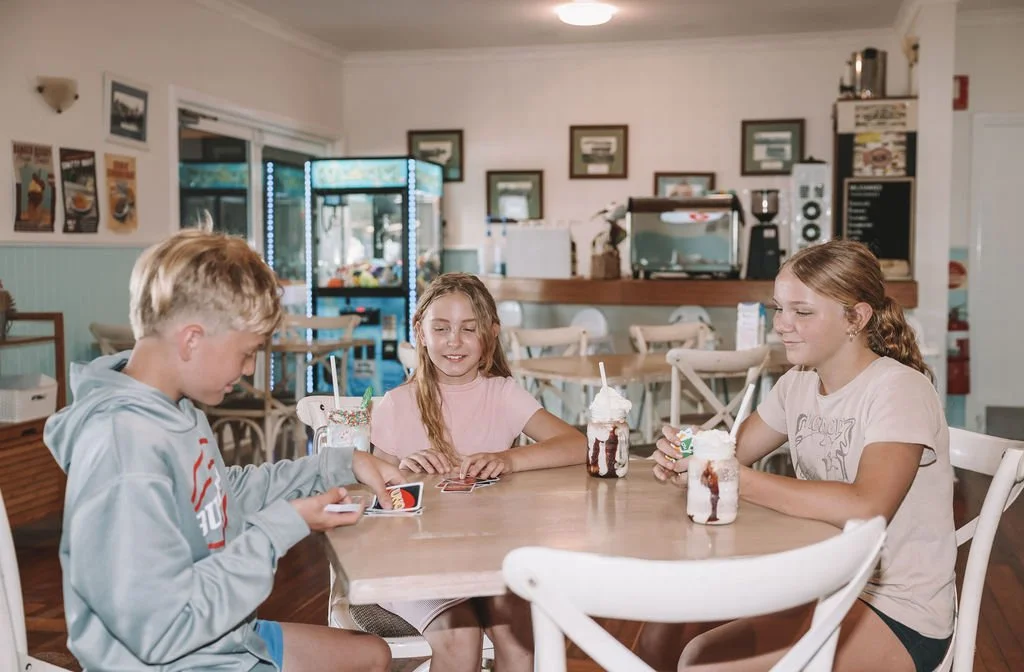 Three children playing cards and drinking milkshakes at a cafe table.