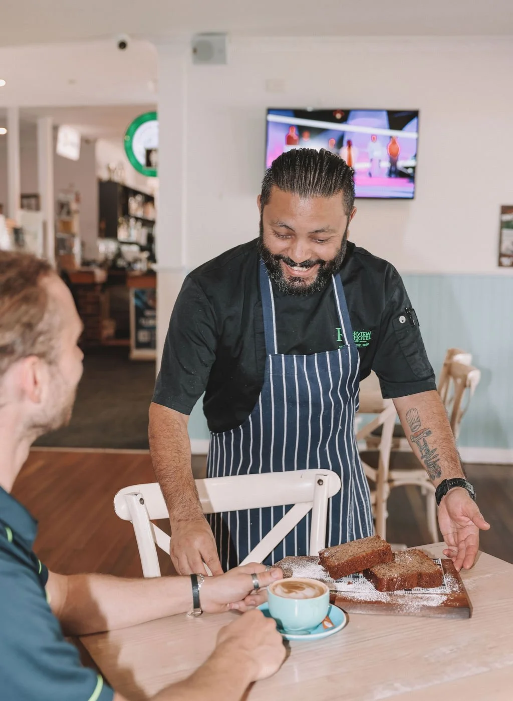 A smiling chef presenting slices of bread or cake to a customer in a restaurant.