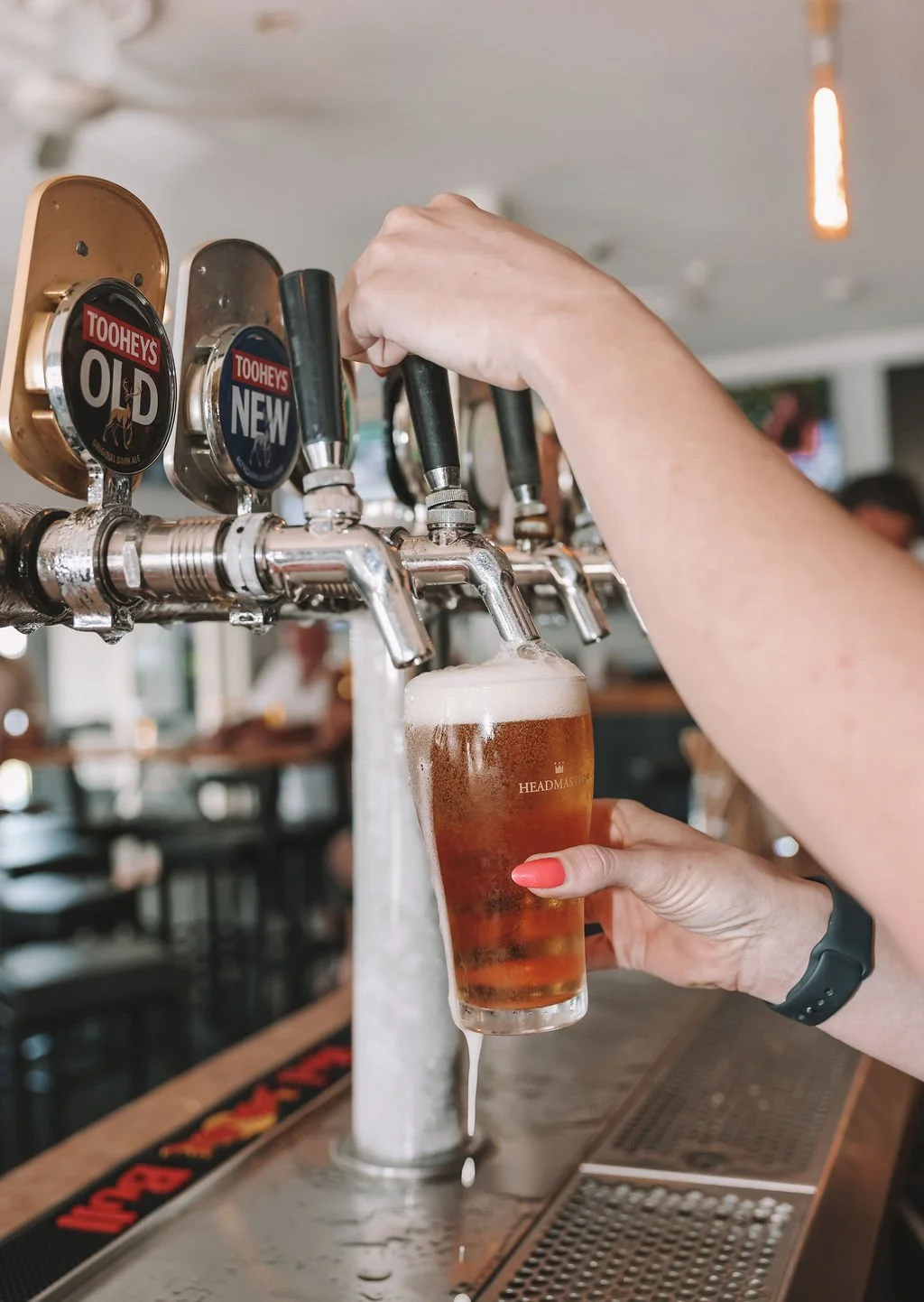 Person pouring beer from tap into a glass at a bar or pub, with multiple beer taps in the background.