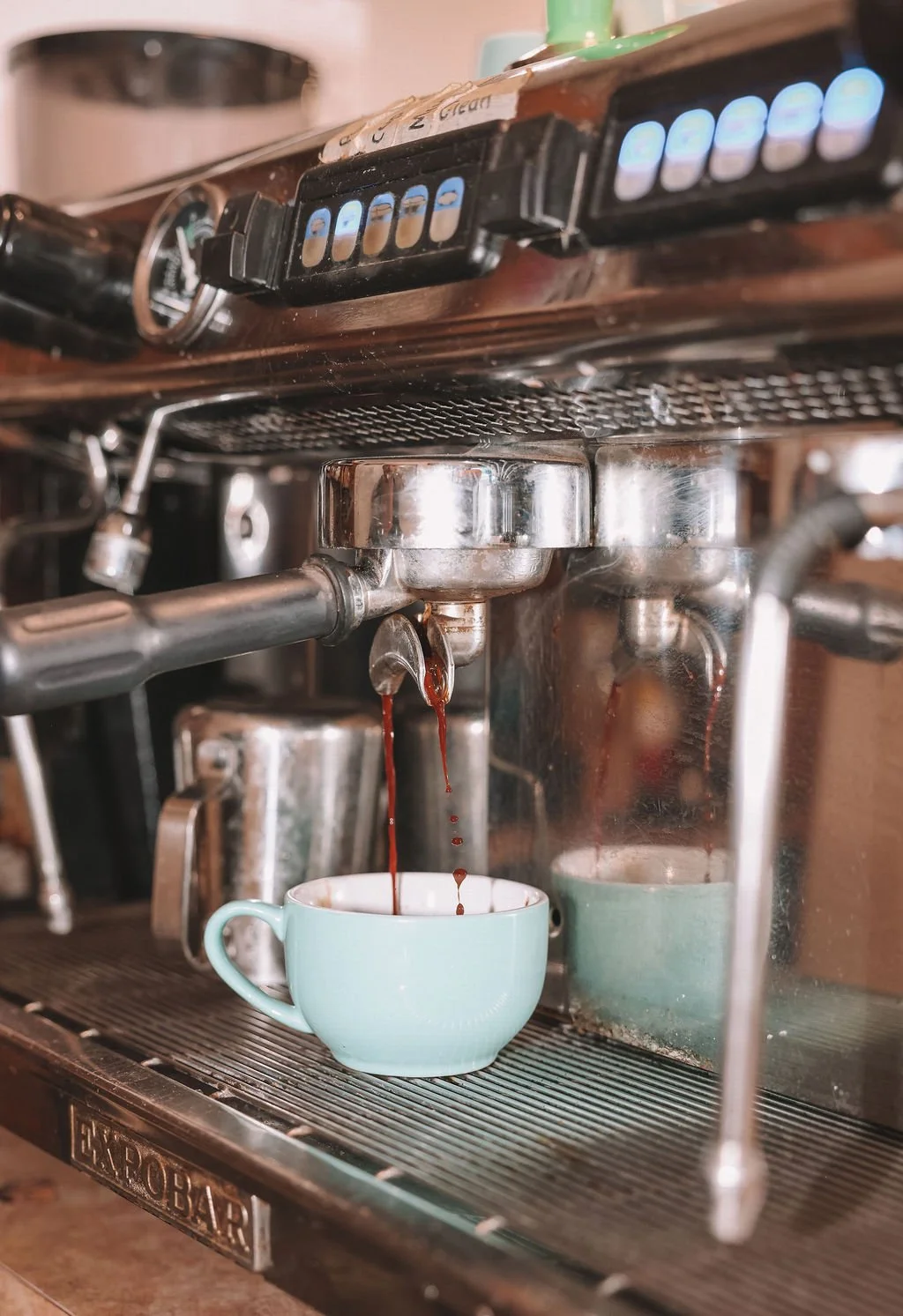 Close-up of a vintage espresso machine brewing coffee into a light blue mug.