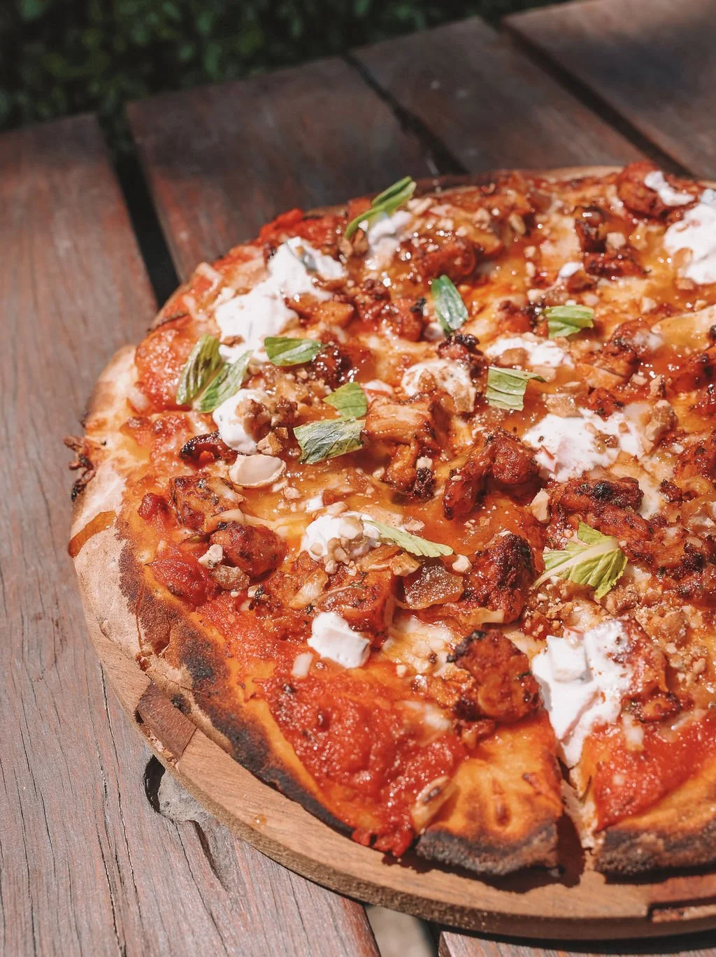 Close-up of a pizza with toppings like cheese, green onions, sausage, and chopped vegetables on a wooden table.