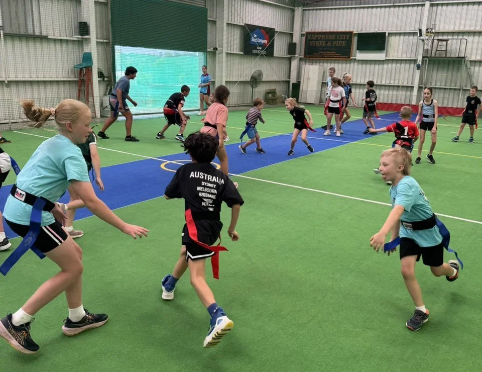 Kids participating in a martial arts training class in an indoor sports facility, wearing uniforms with colored belts.