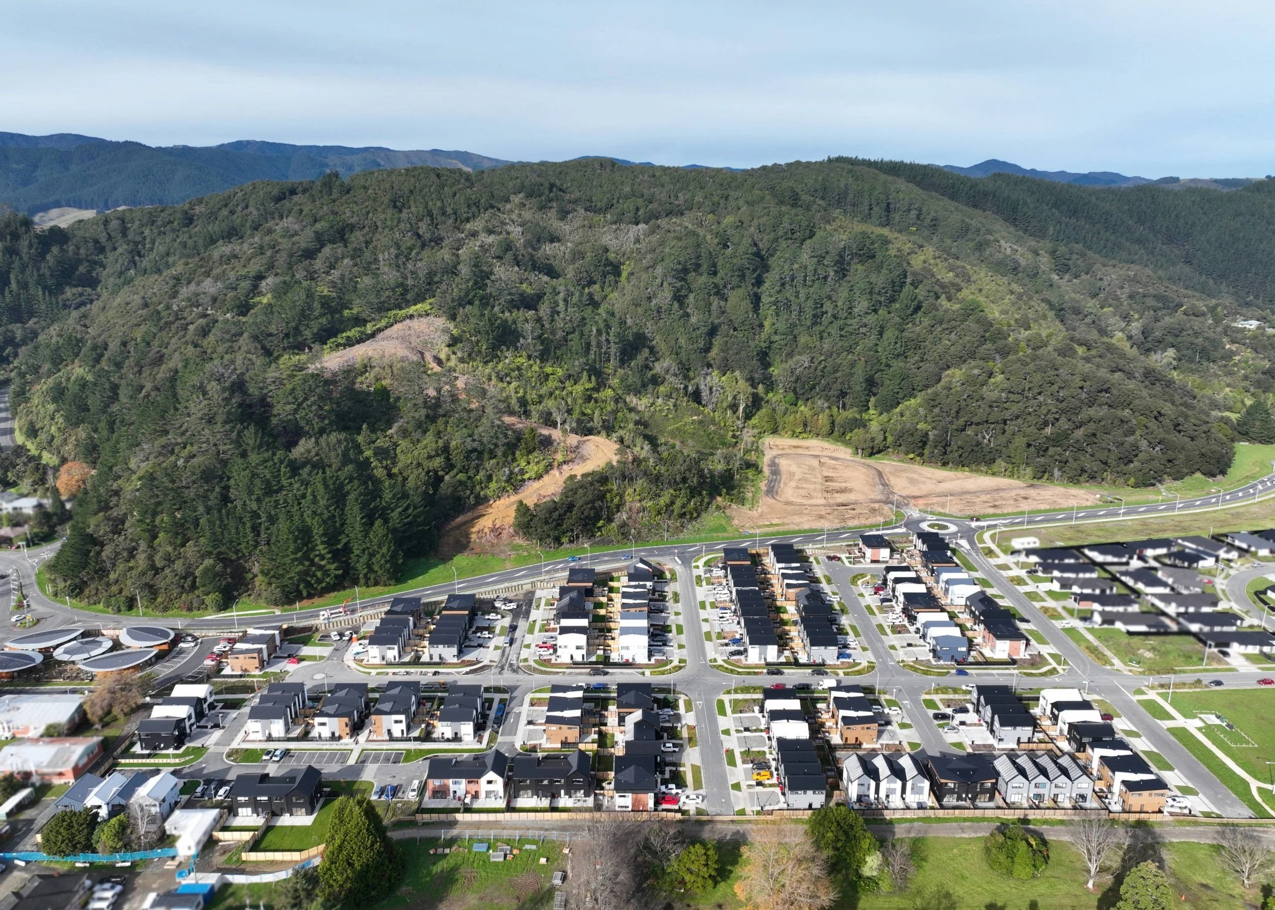 Aerial view of Wallaceville Estate by Gillies Group, shows a residential neighbourhood with modern houses and streets at the base of forested hills.
