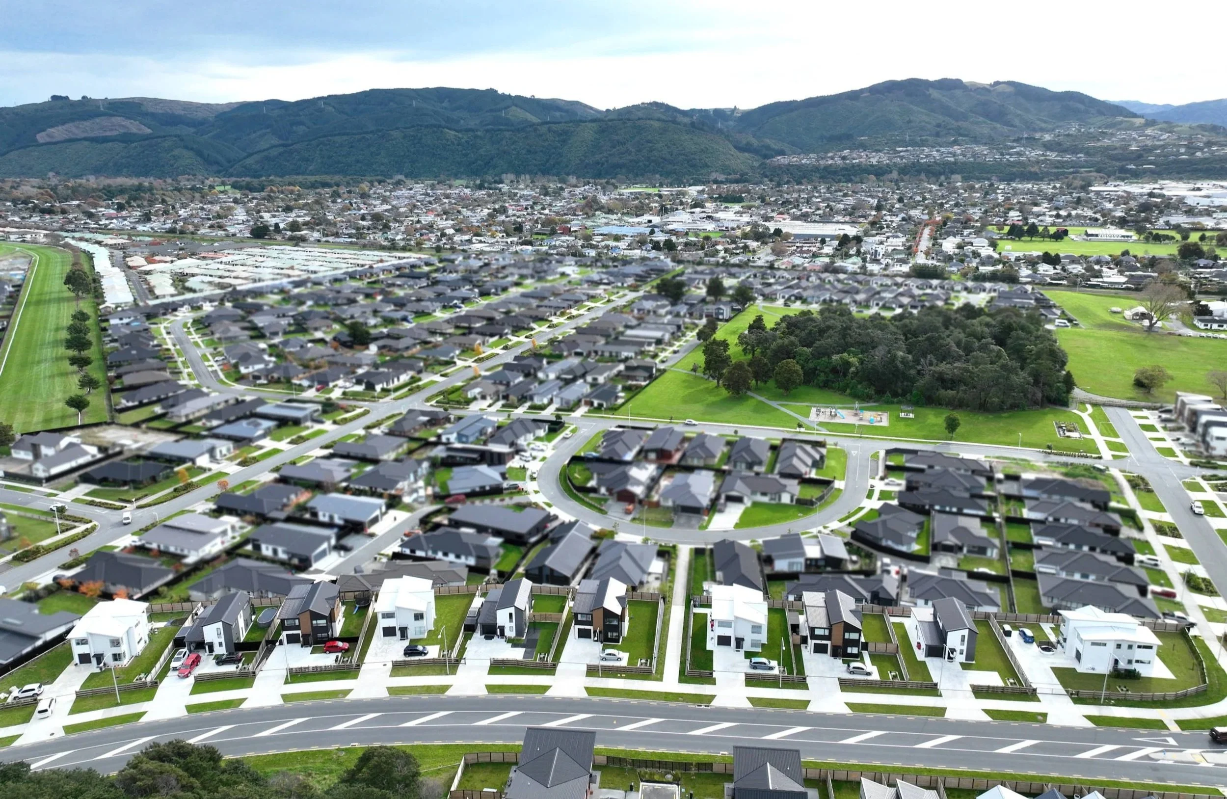 Aerial view of Urban Precinct in Wallaceville Estate features a suburban neighbourhood with houses, roads, and green spaces, with mountains in the background.