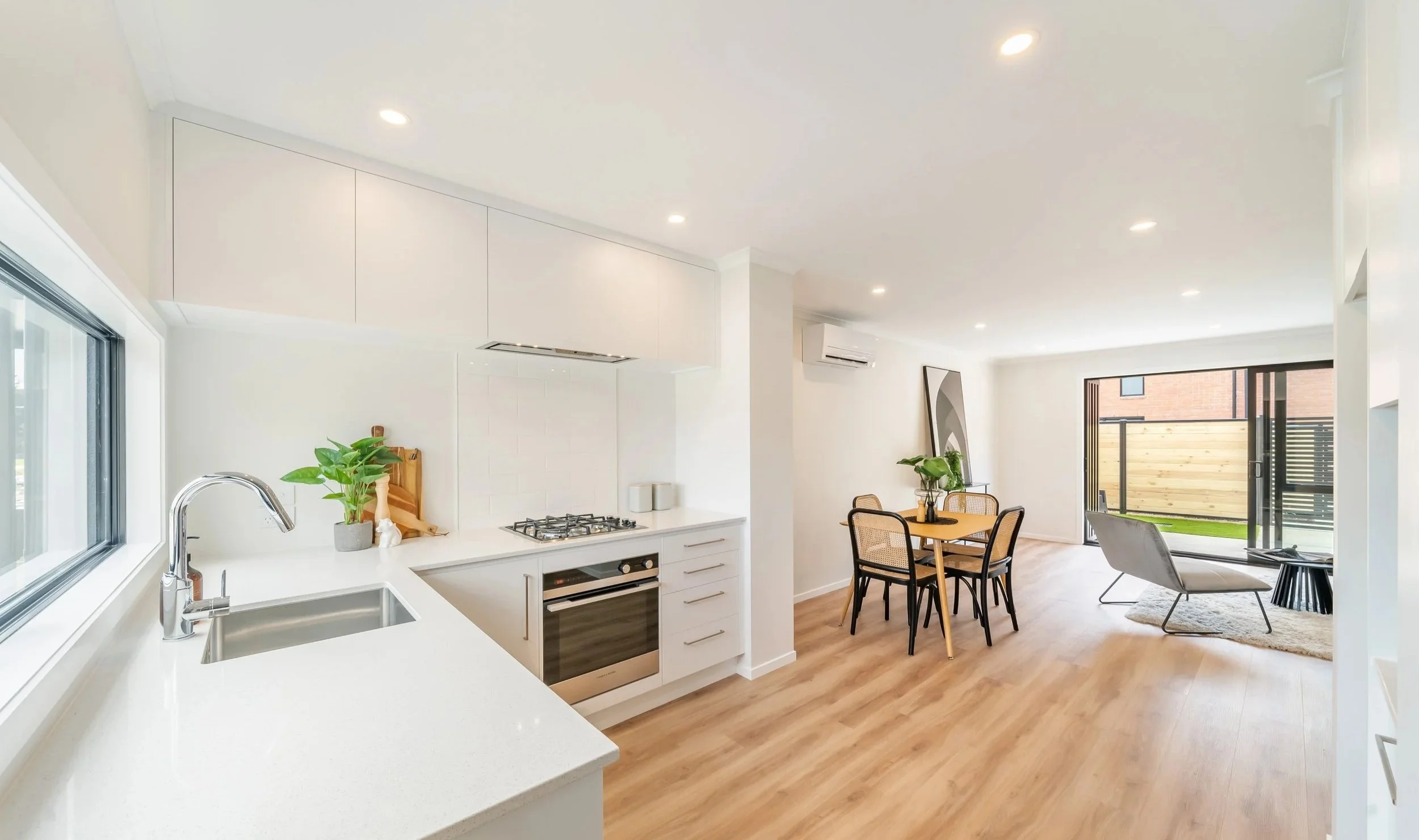 Modern open-concept kitchen and living area with white cabinets, wooden floors, and large sliding glass door leading to an outdoor space.