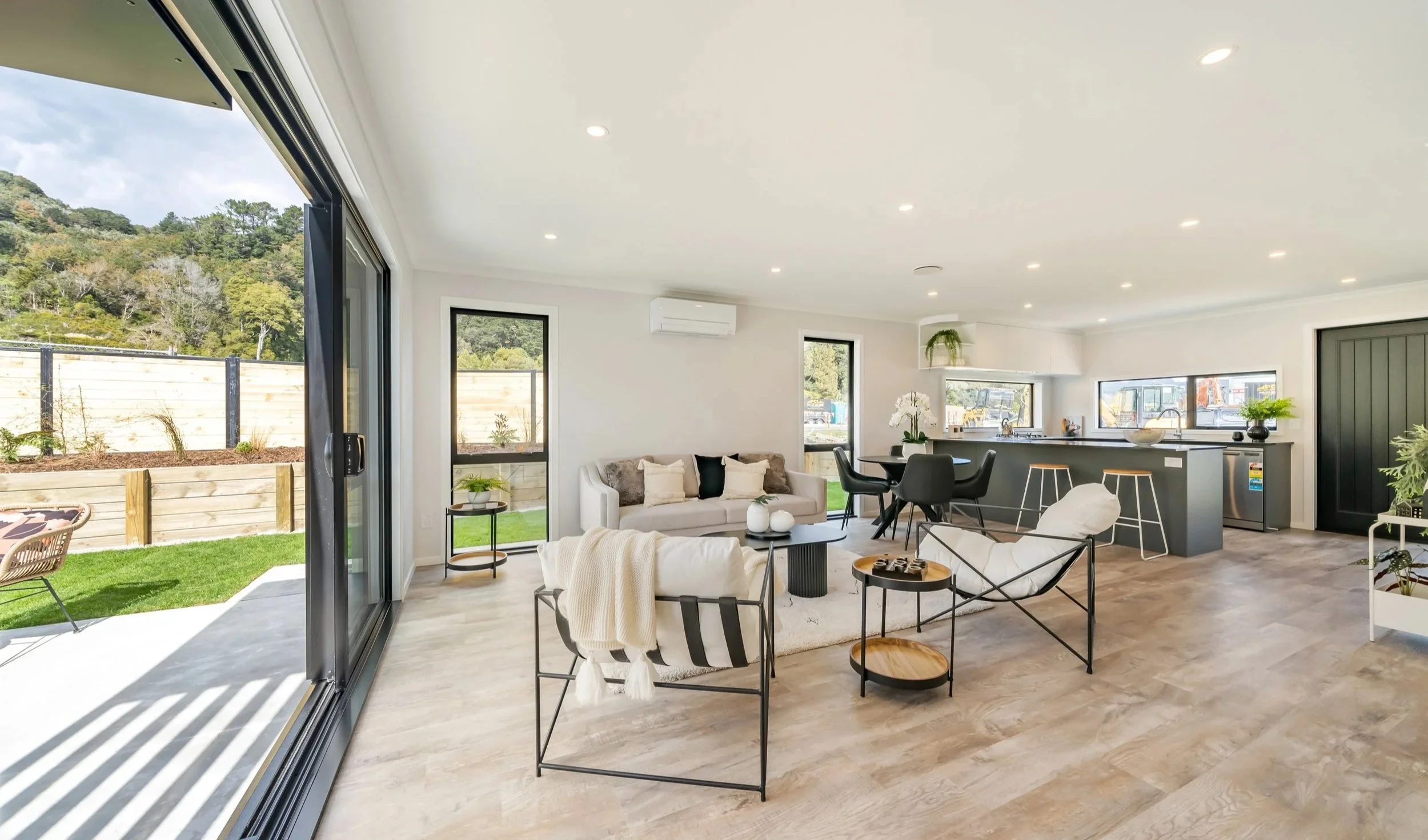 Modern open-concept living room with large sliding glass doors opening to a green outdoor space, featuring a neutral color palette, minimalist furniture, and natural light.