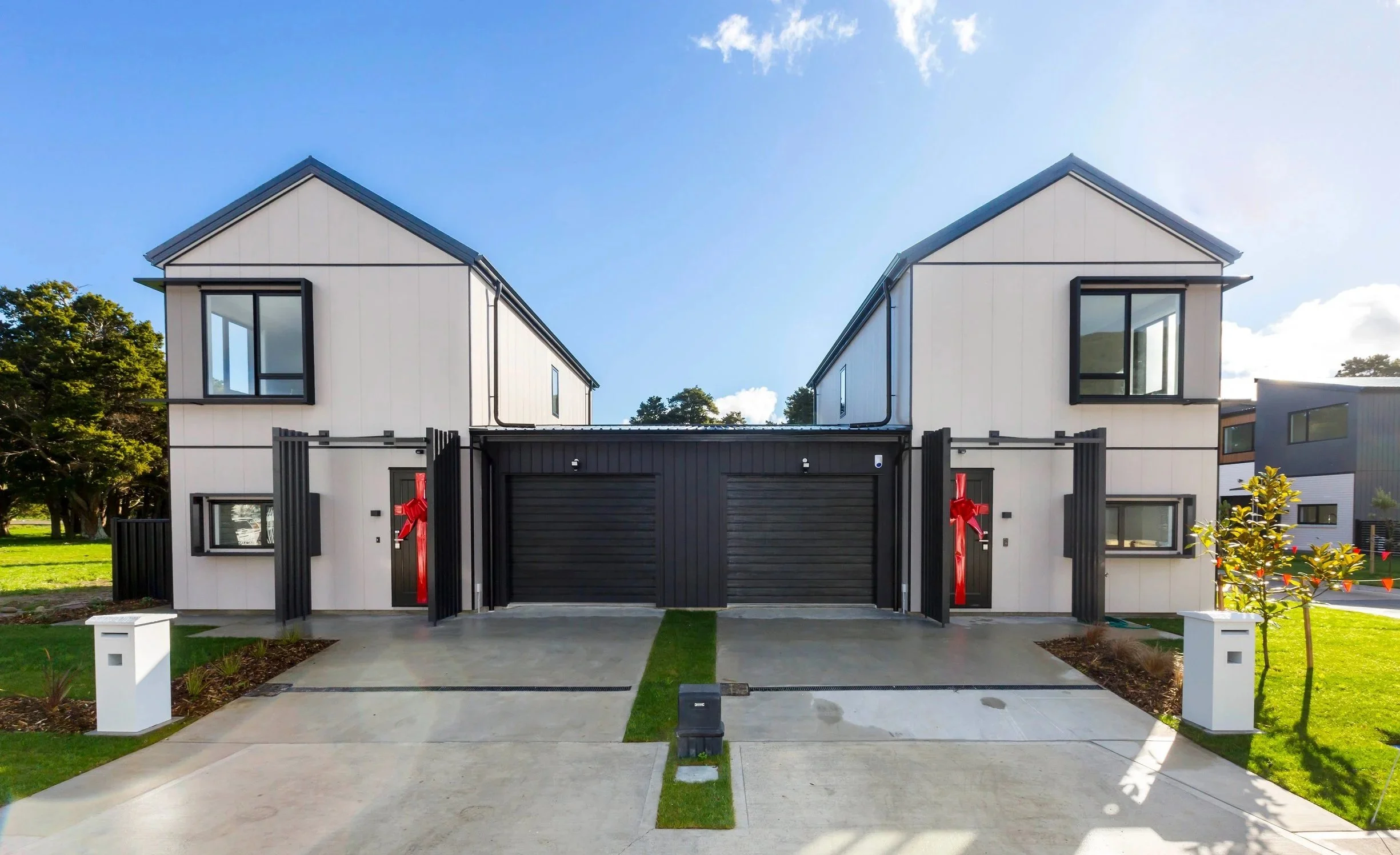 The Reserve: Final Release houses in the Type E style, with black garages and red bows on the doors, overlooking a driveway with a central strip of grass and mailbox posts.