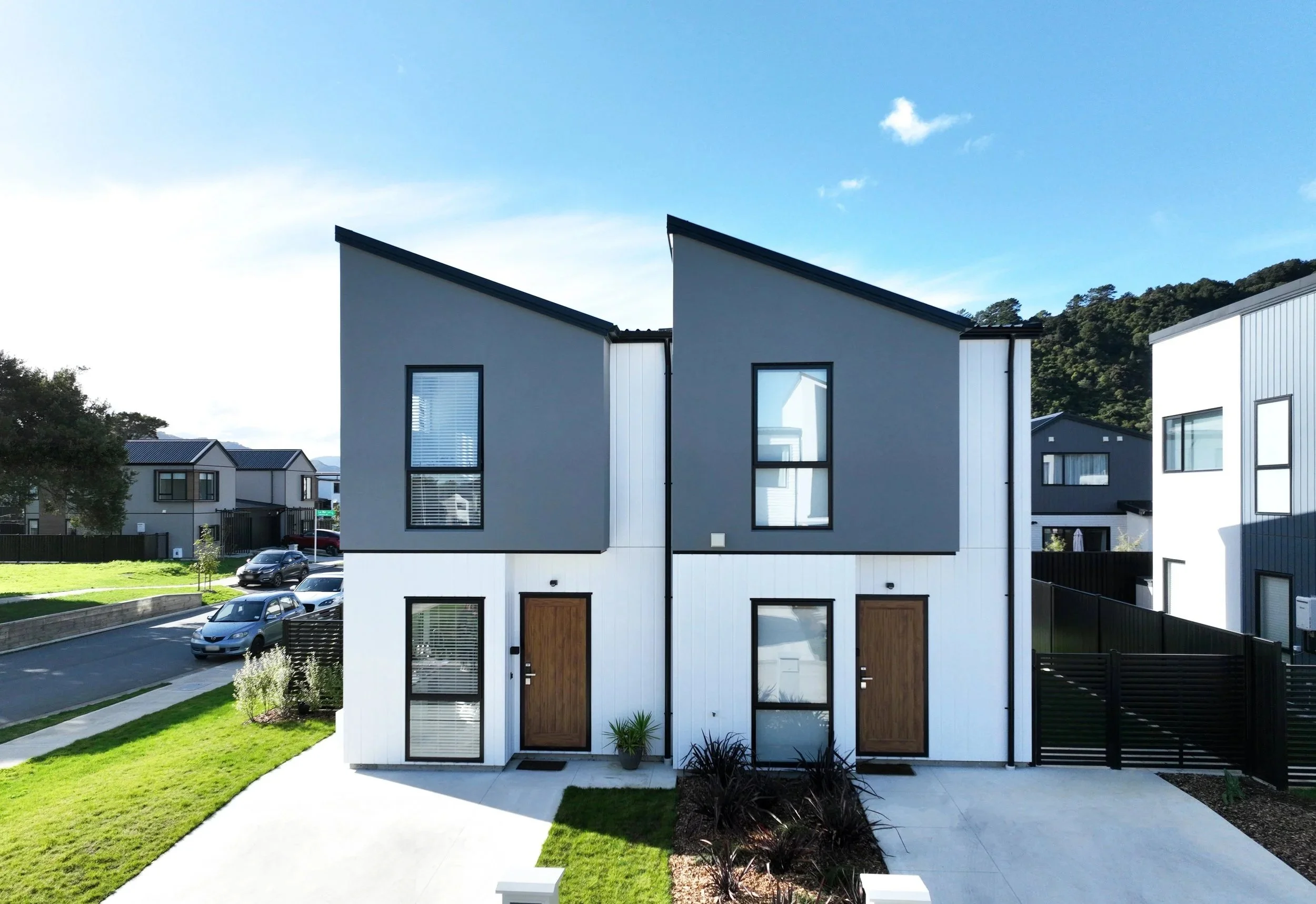 Two modern Type A townhouses with gray upper sections and white lower sections, large windows, and wooden front doors in a suburban neighbourhood with cars on the street and green lawns, located in The Reserve: Final Release by Gillies Group.