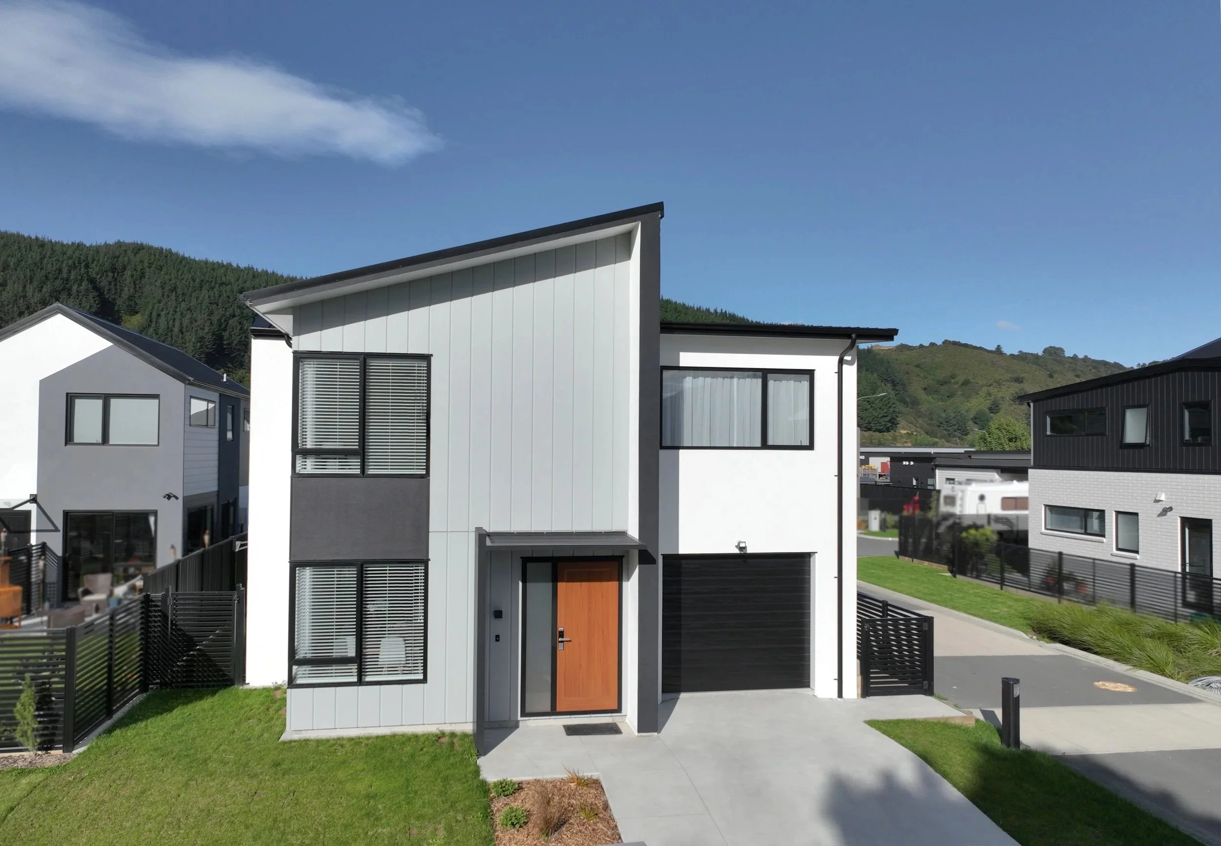 Type G standalone house within Gillies Group's The Reserve, with black accents and large windows, located in a suburban neighbourhood with green lawns and similar style houses, with hills and blue sky in the background.