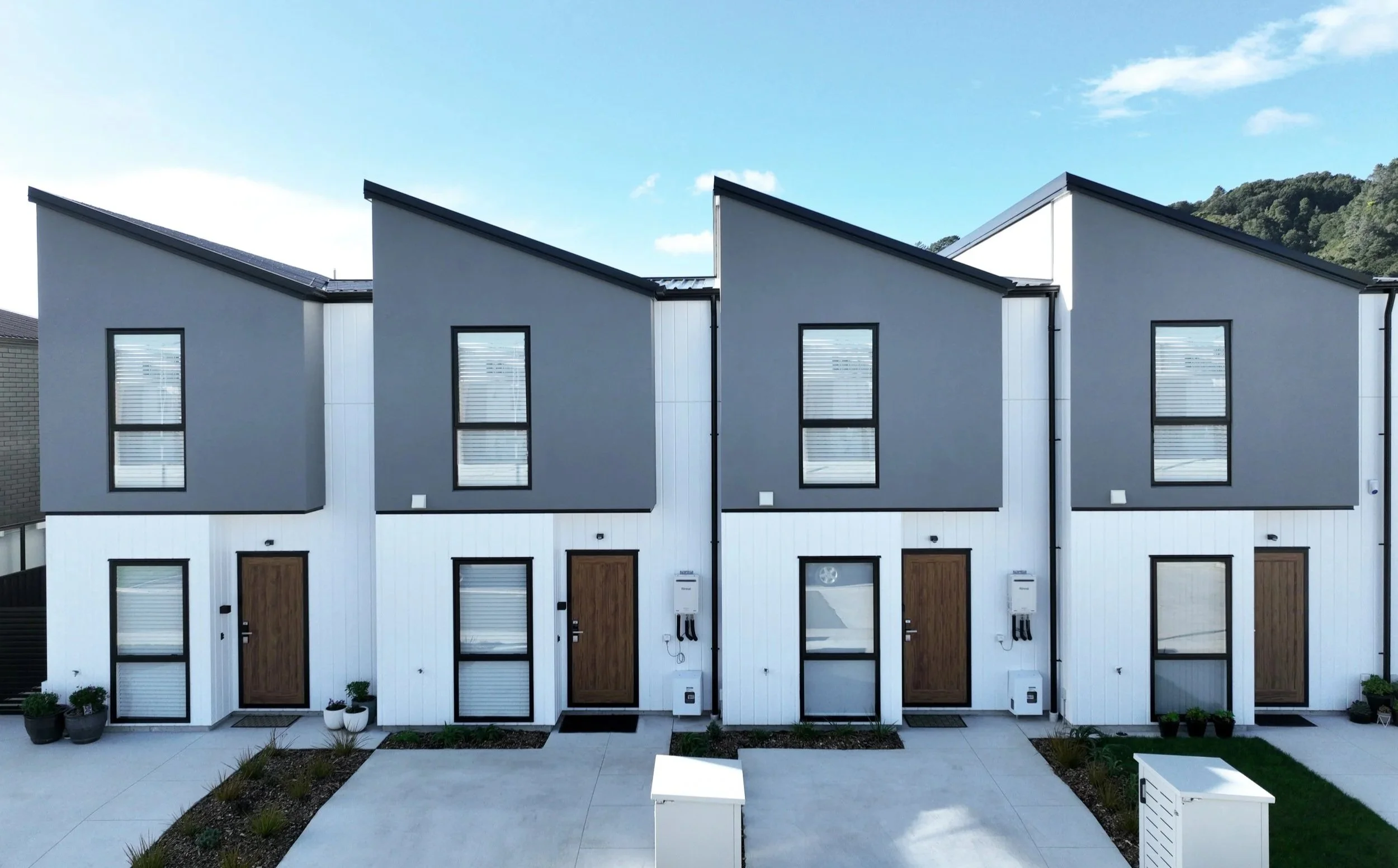 Row of four Type A townhouses with gray upper floors, white lower floors, brown doors, and large windows, under a clear blue sky.