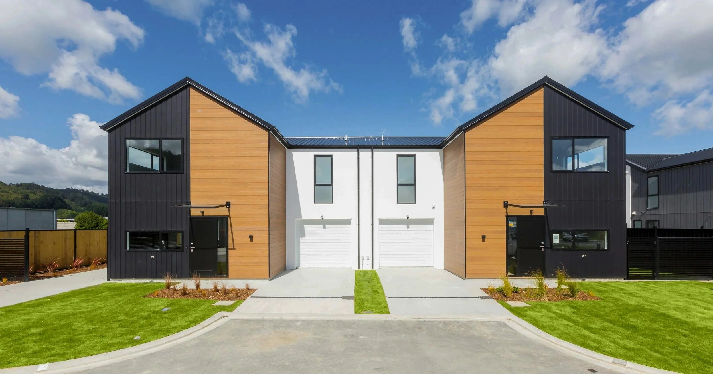 Type F houses with black and wood exterior, white garage doors, green lawns, and a cloudy sky, located in Wallaceville Estate, a development by Gillies Group.