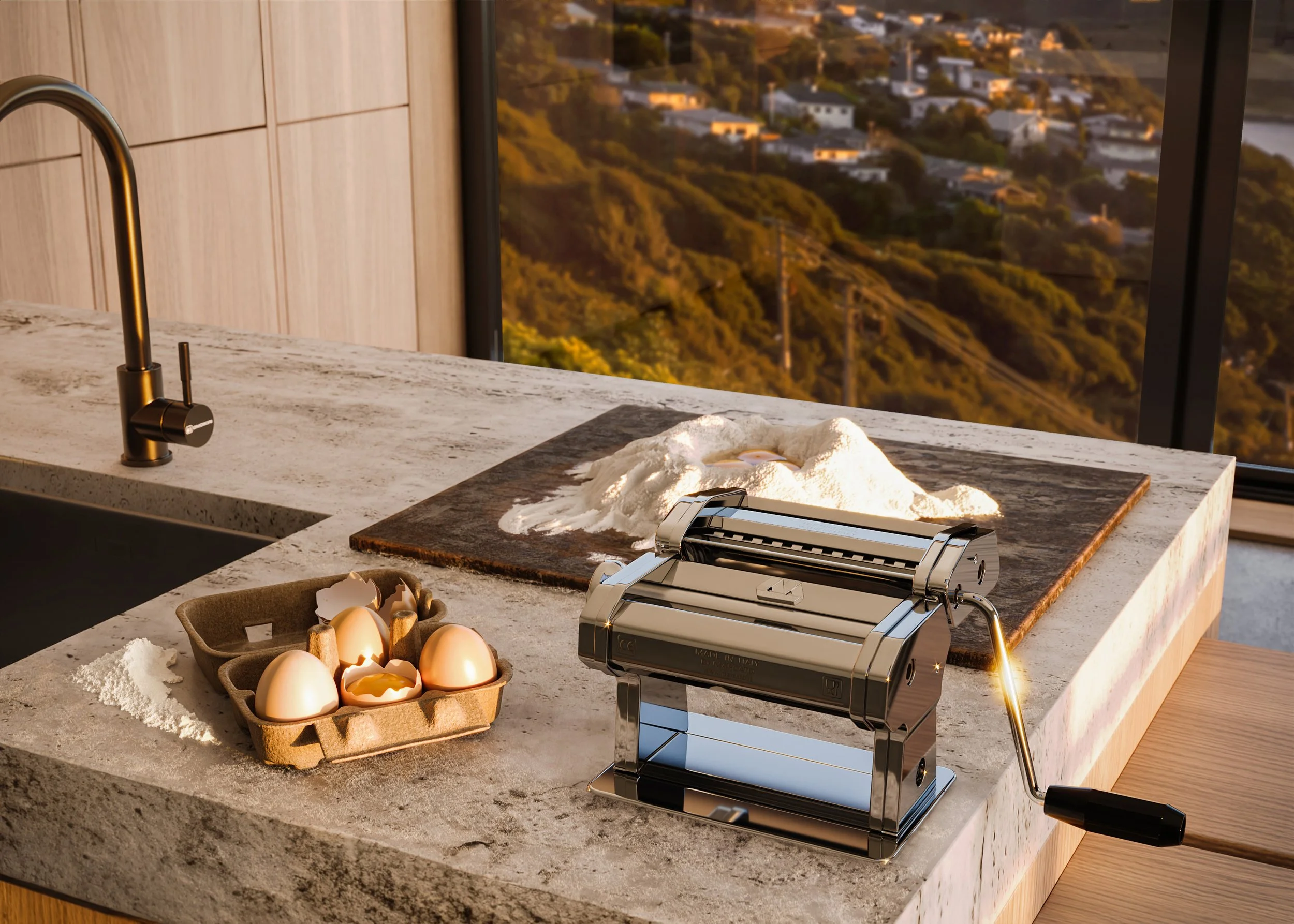 Kitchen countertop with a pasta maker, a tray of eggs, and a mound of flour with a rolling pin, overlooking a scenic landscape through a large window.