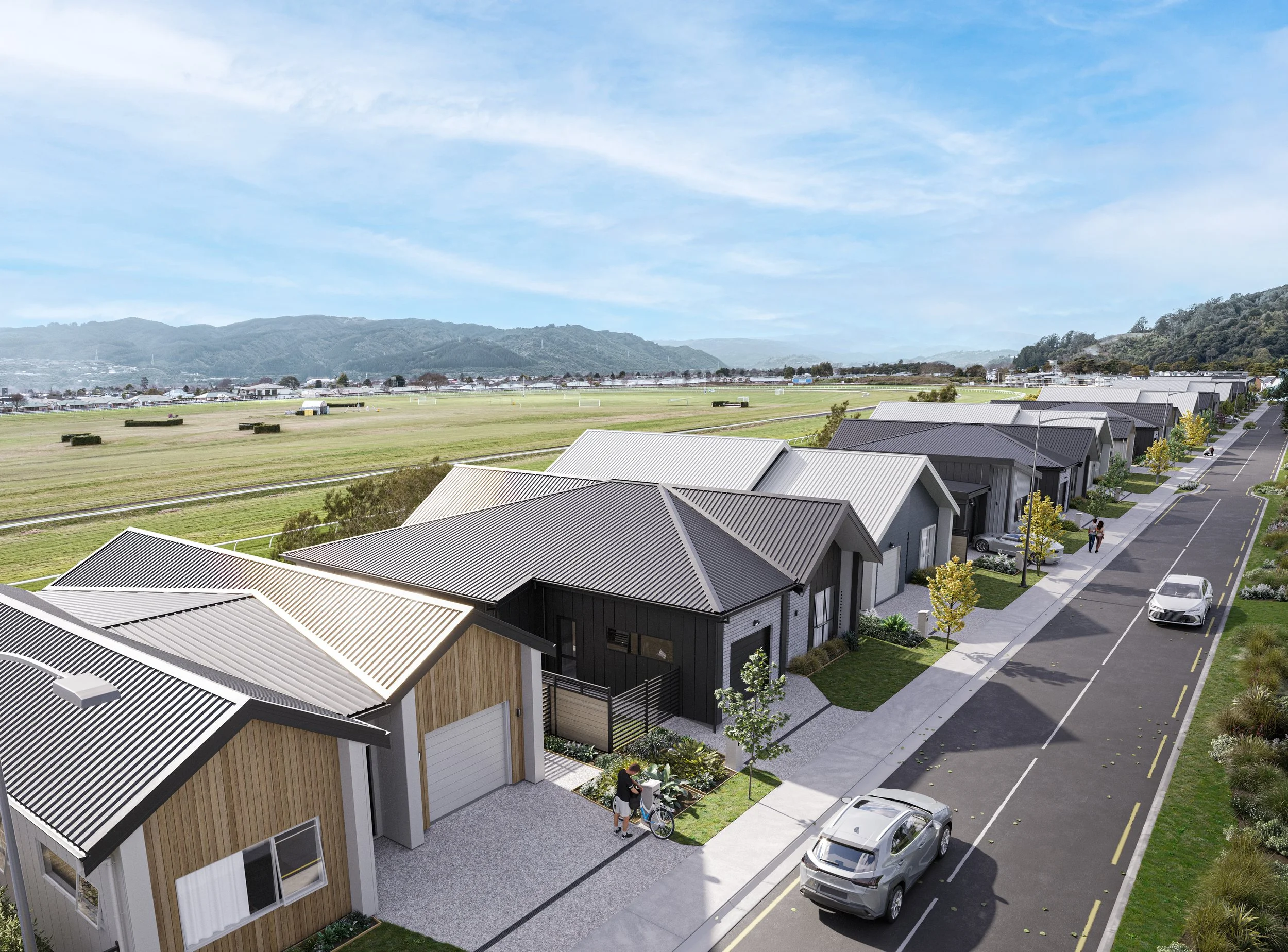 A row of Back Straight homes along a quiet street with parked cars, trees, and people walking, with open fields and distant hills in the background under a cloudy sky.
