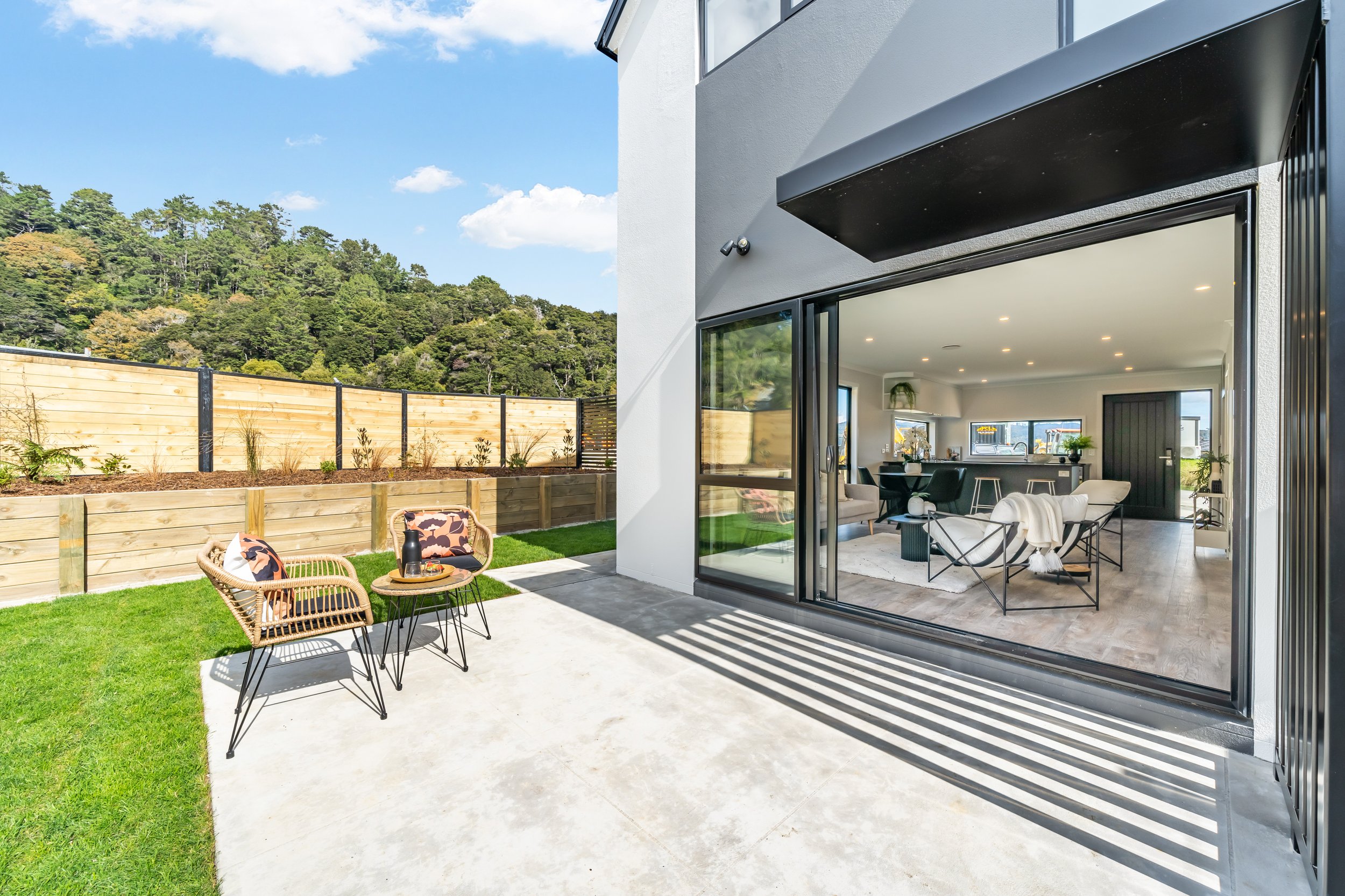 Modern house with a spacious backyard patio, outdoor seating, wooden fence, and lush green lawn, located in The Reserve in Wallaceville Estate.