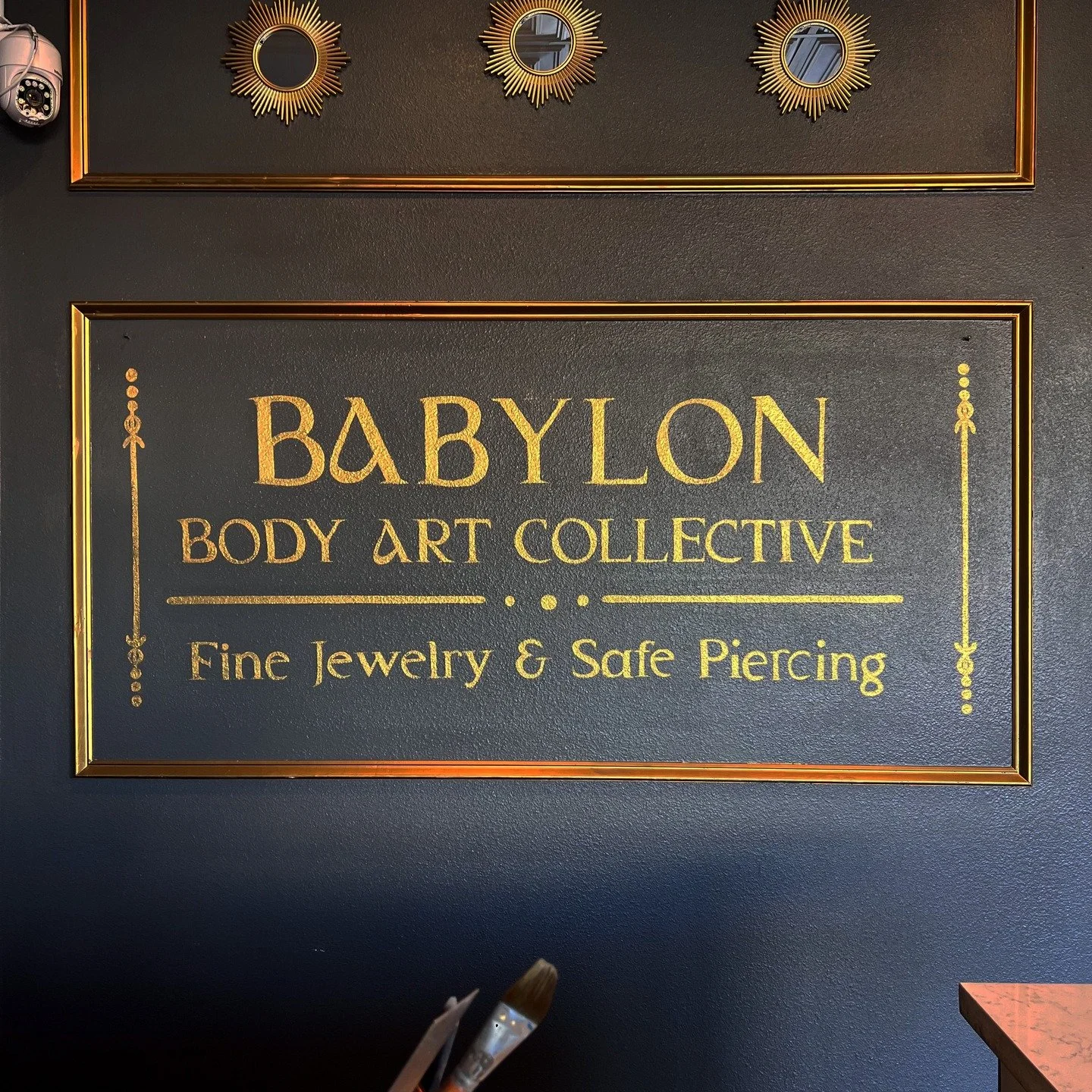 Quick lettering piece for @babylon_bodyart done in February 2025. Lettering is based in a red toned brown to cancel out the blue toned wall, then finished with multiple coats of gold to match the details throughout the rest of their shop! Layout and 